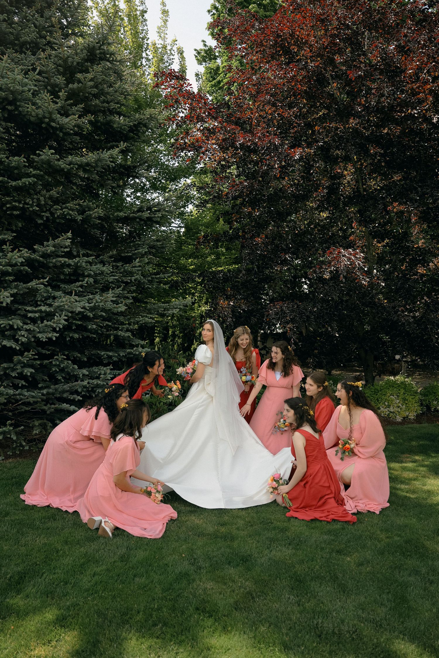 Bridal party with bridesmaids in coral dresses posing on green lawn.