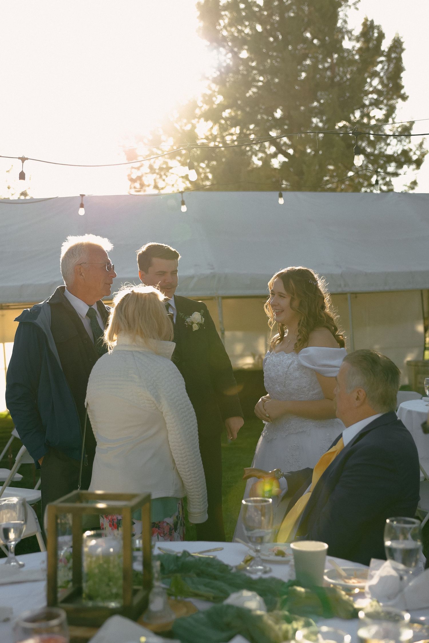 Wedding guests and bridal party mingling at sunset during an outdoor reception.