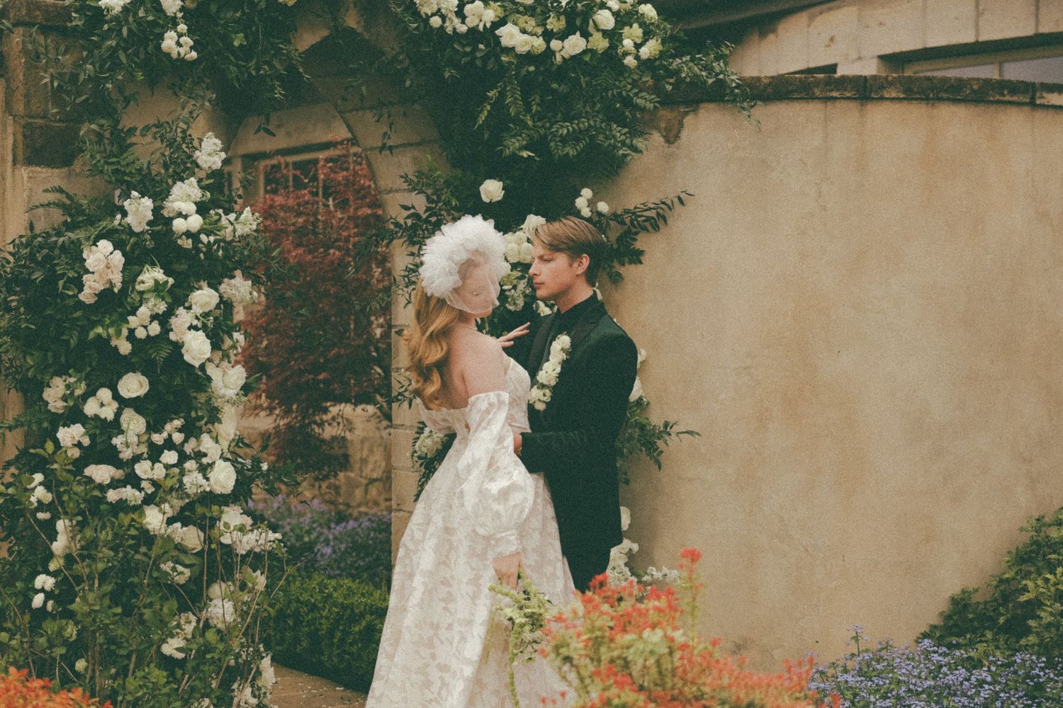 Wedding couple poses under an archway adorned with white roses and greenery.