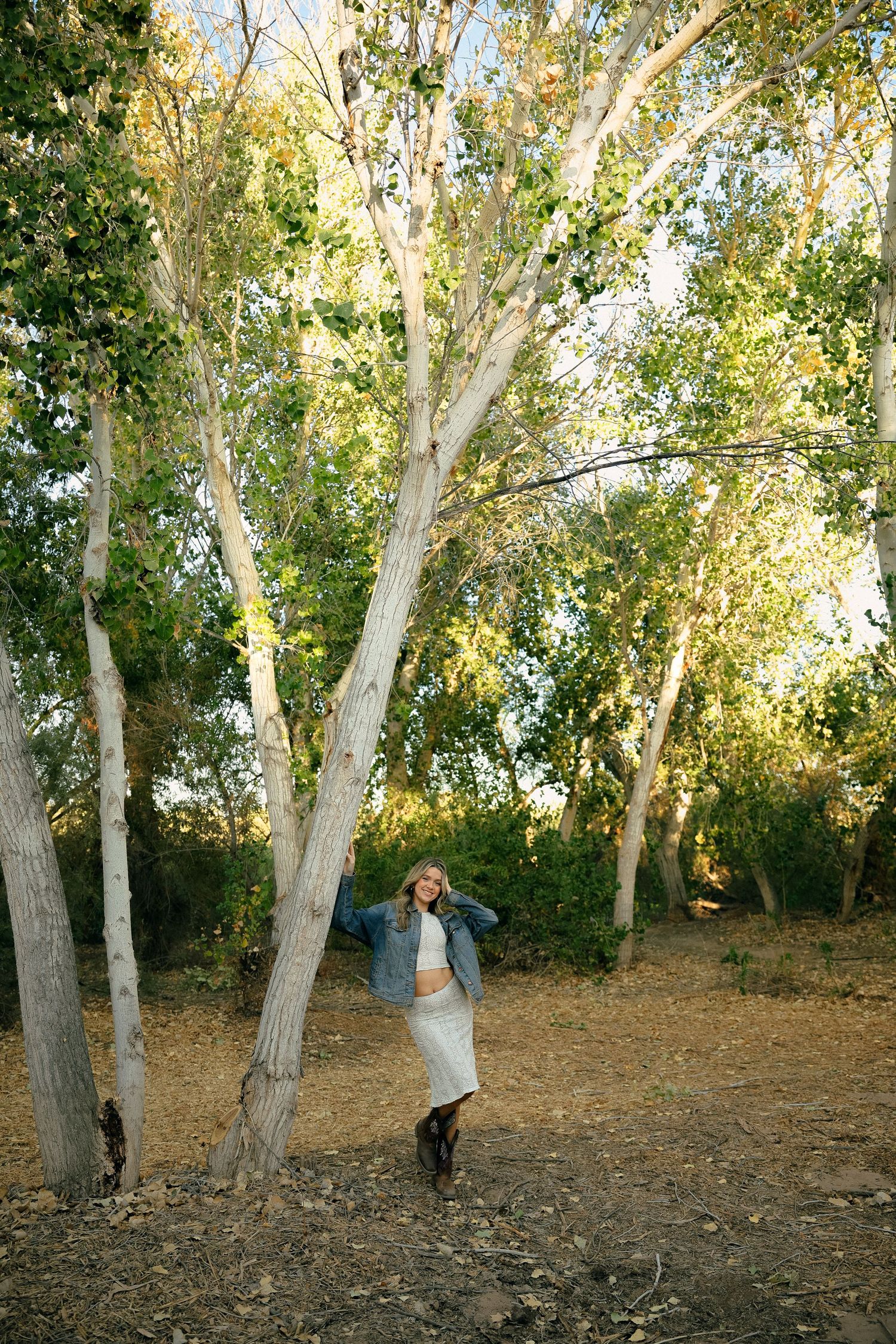 A person dances playfully among tall white birch trees in a natural forest setting.