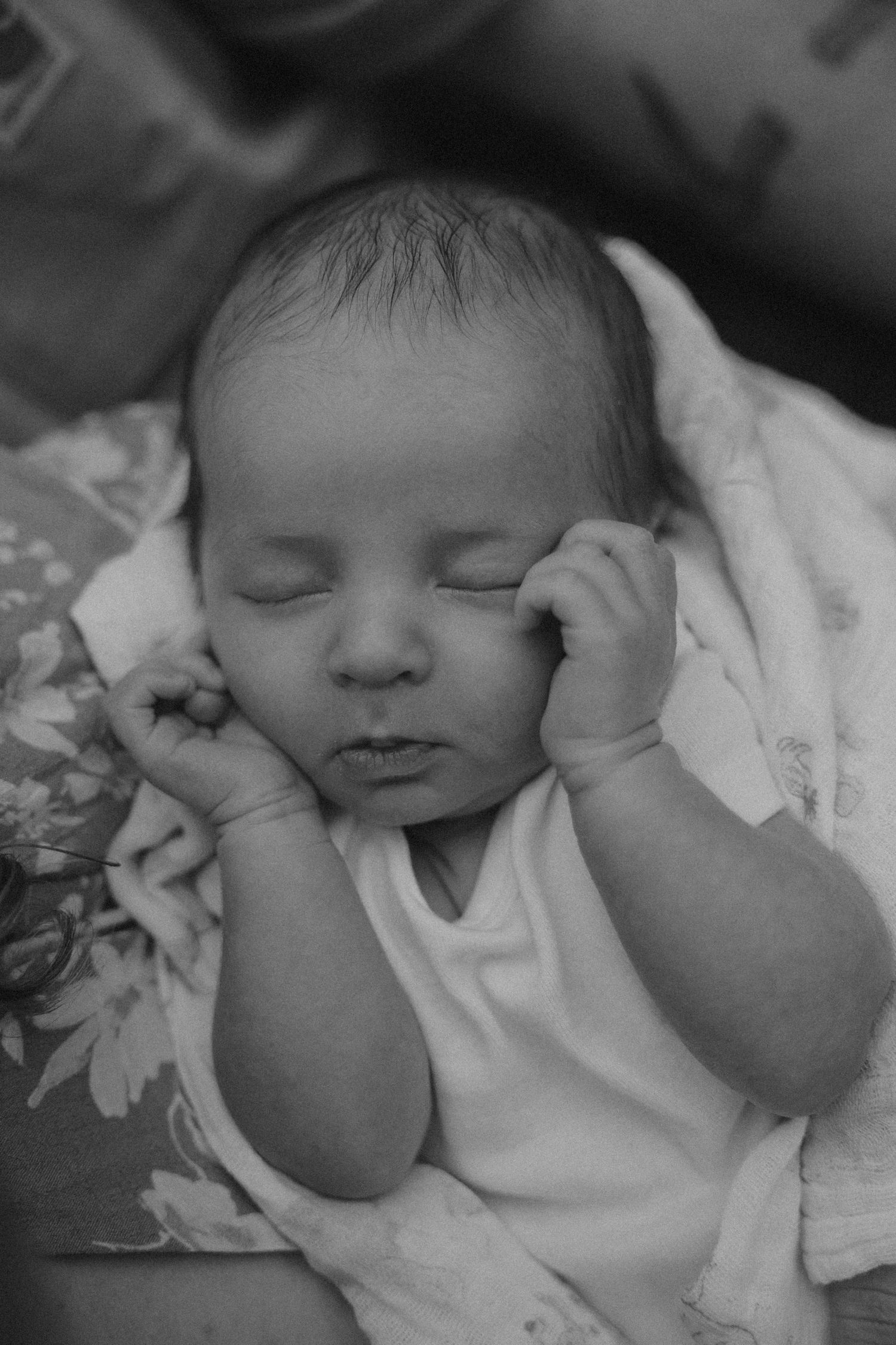 A newborn baby stretches and yawns while lying on white fabric in black and white.