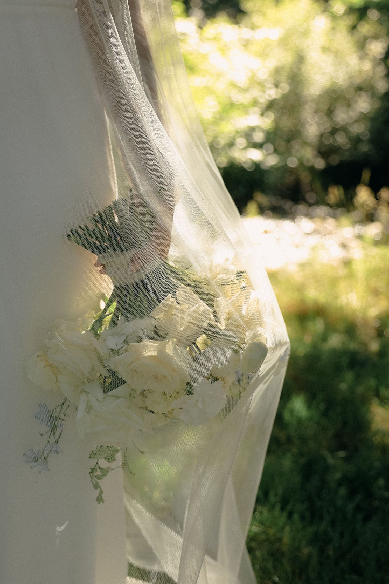 Elegant white wedding dress with delicate floral details captured in soft sunlit garden setting.