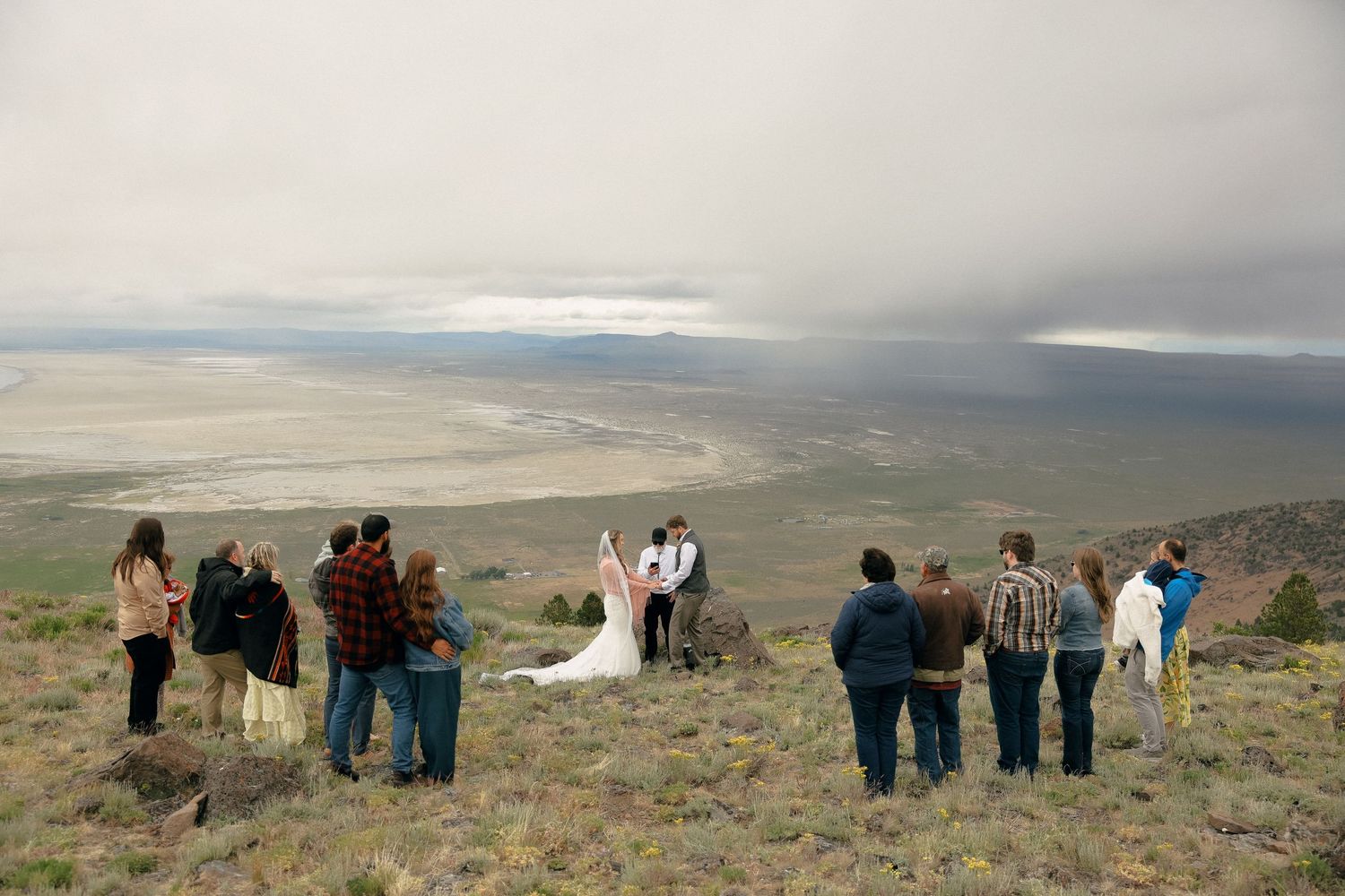 A panoramic sequence showing a group of people looking out over a vast mountain landscape on an overcast day.