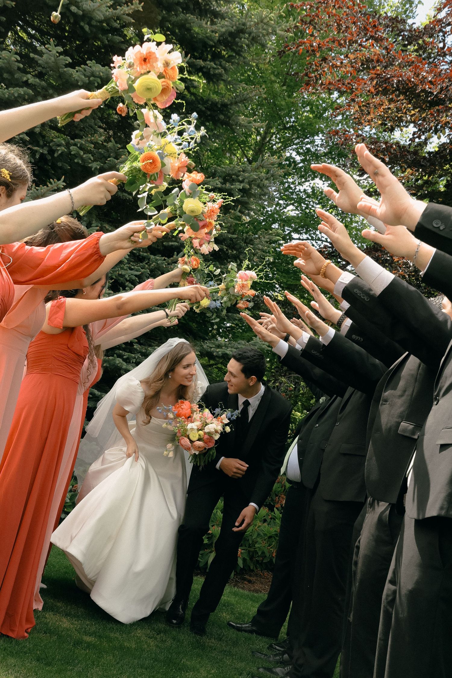 Wedding party with bridesmaids in coral dresses and groomsmen throwing flower petals outdoors.