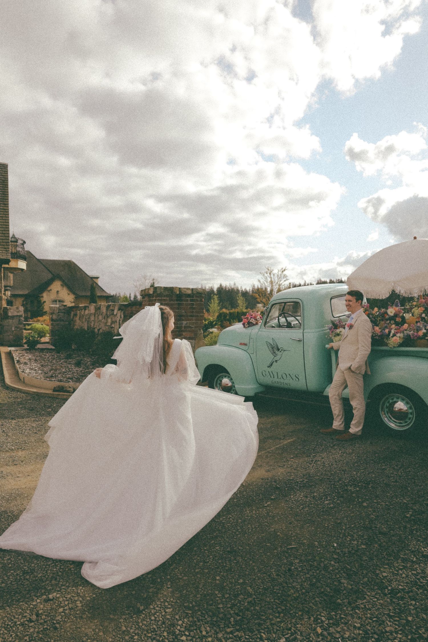 Wedding party poses with vintage mint green truck under cloudy skies.