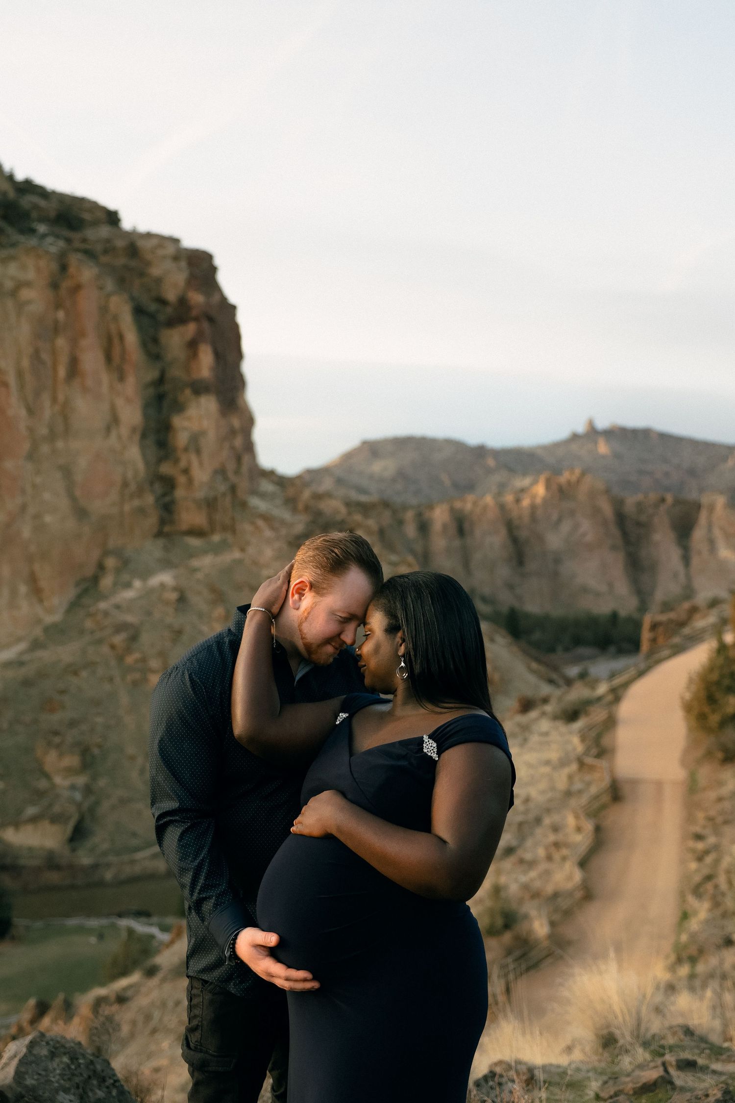 A couple shares an affectionate moment against a backdrop of dramatic desert cliffs.