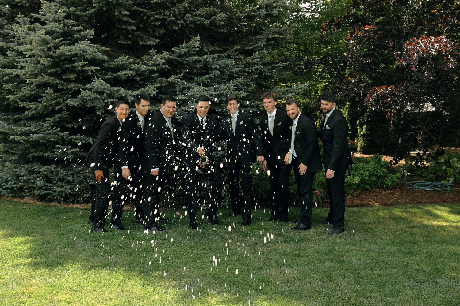 Wedding party celebration with confetti toss in garden setting.