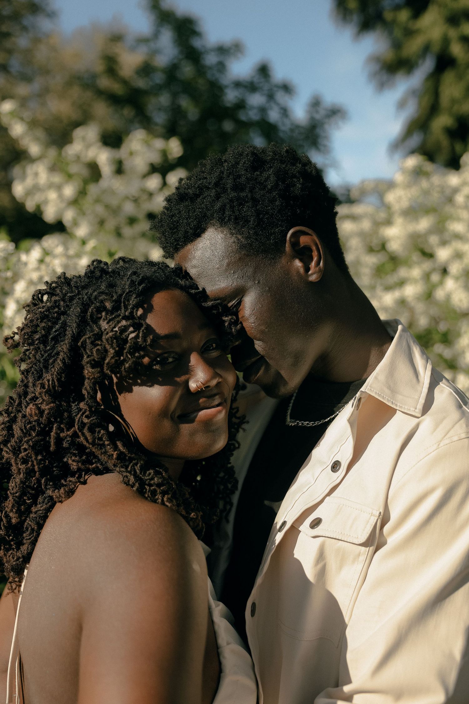 Intimate couple portrait in warm sunlight with flowering trees in background.