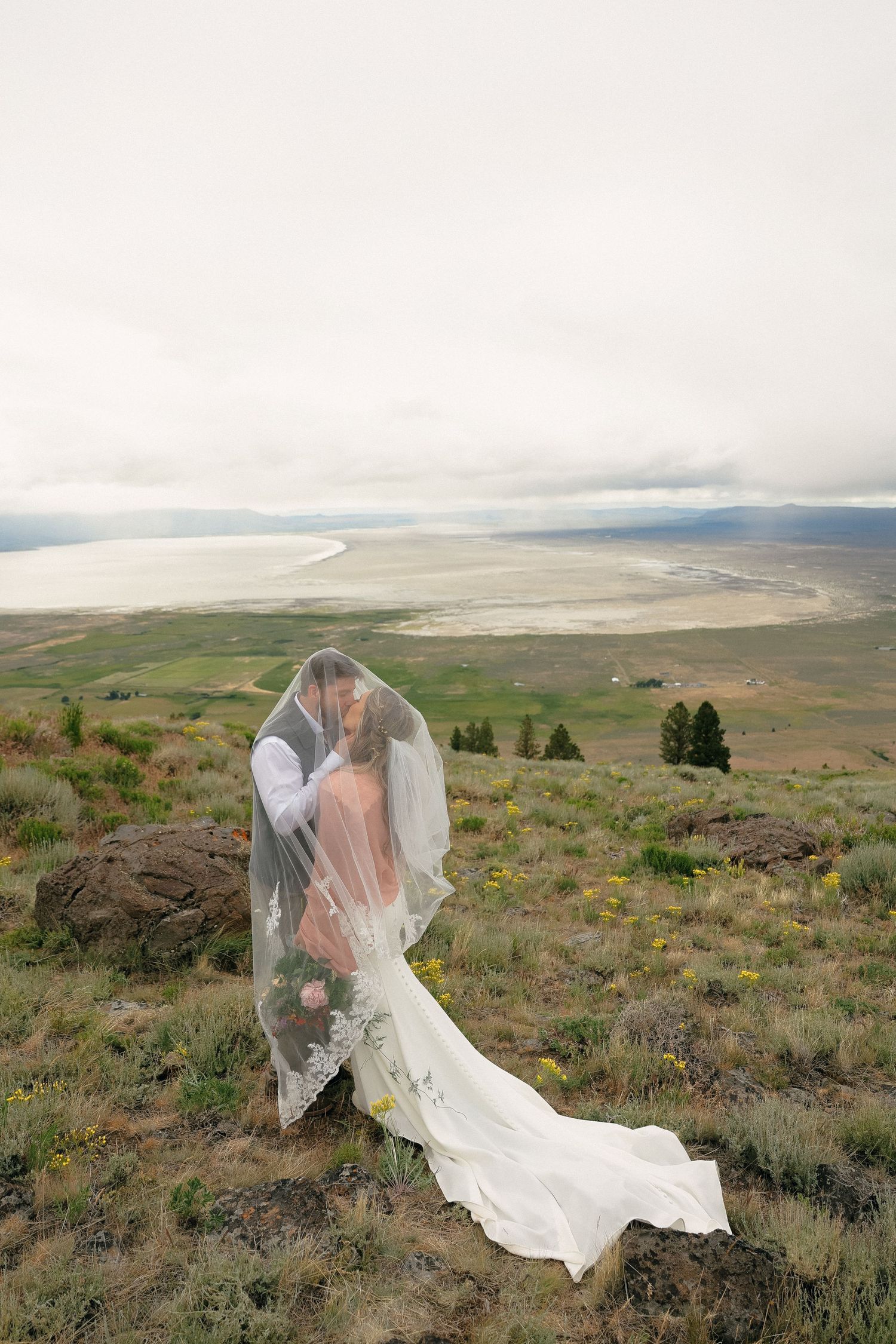A couple shares an intimate wedding moment atop a scenic hillside with a dramatic landscape view in the background.