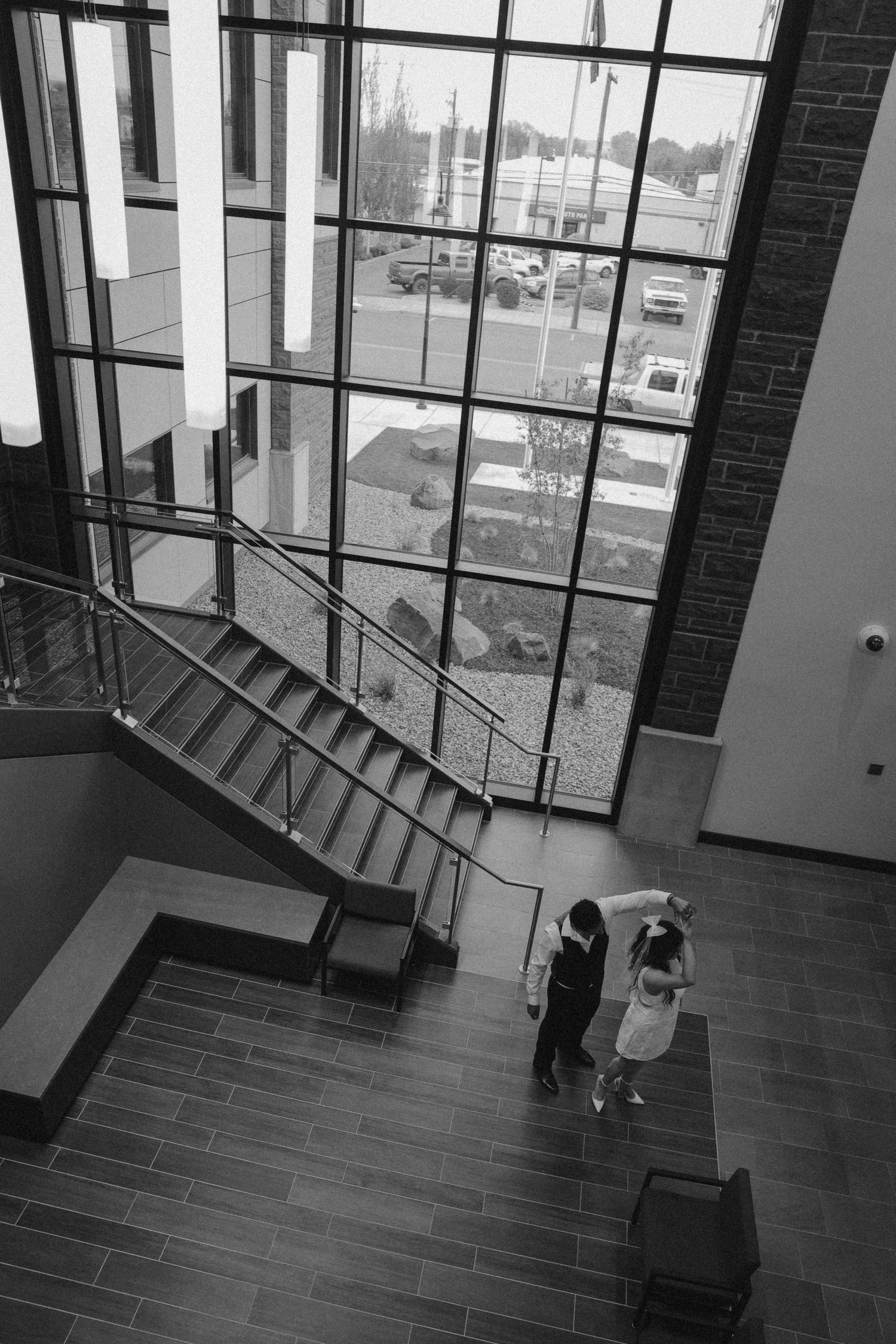 Black and white architectural wedding photo with couple descending modern staircase by large windows.