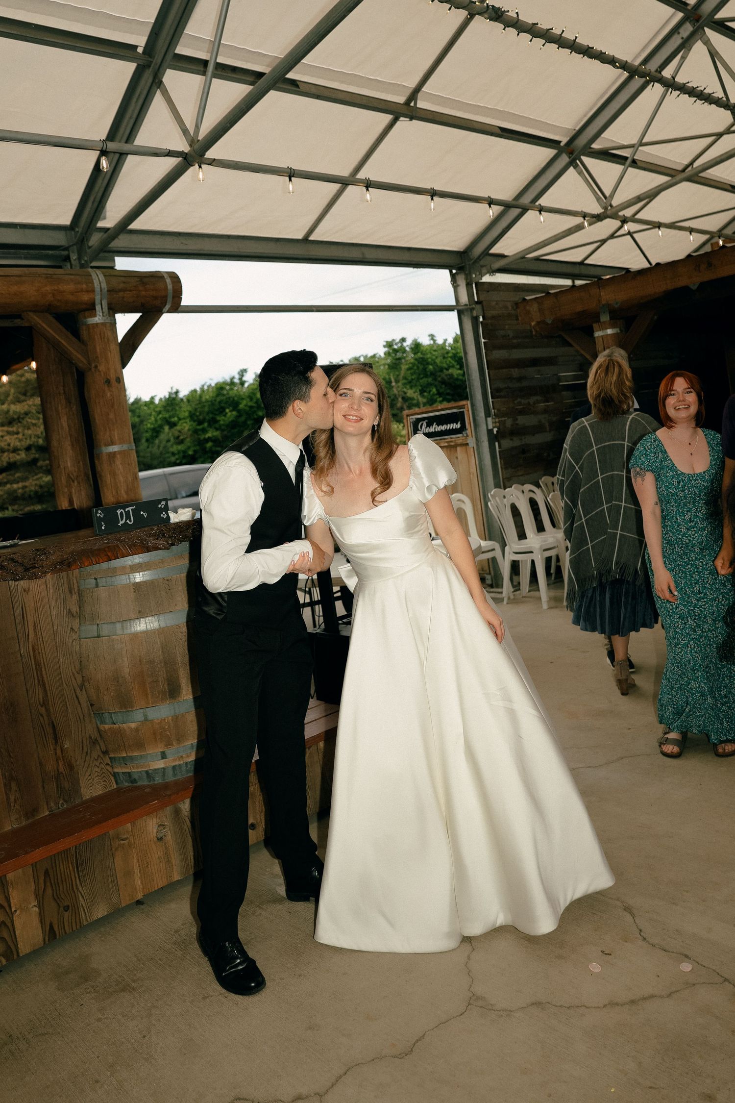 Wedding celebration under a covered pavilion with rustic wooden barrels.
