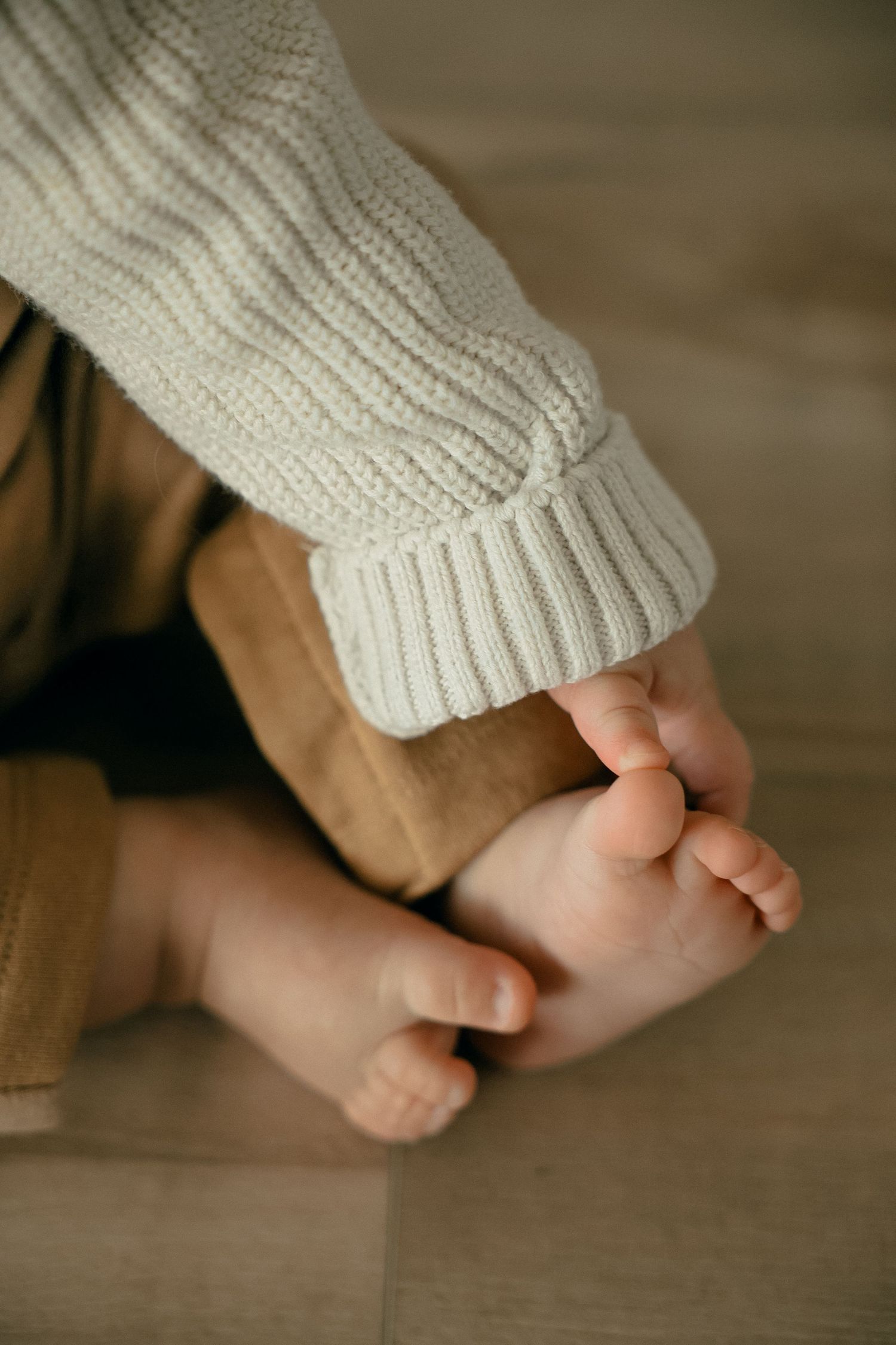 Close-up of tiny baby feet being touched by someone wearing a cream knit sweater.