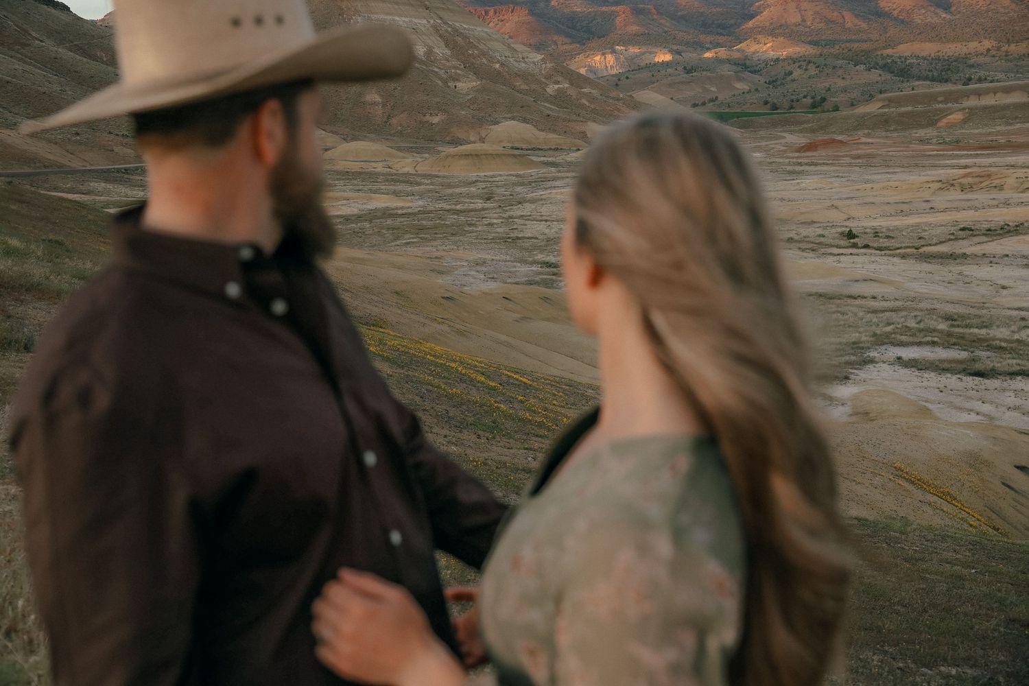 A couple stands together overlooking a scenic mountainous desert landscape at dusk.