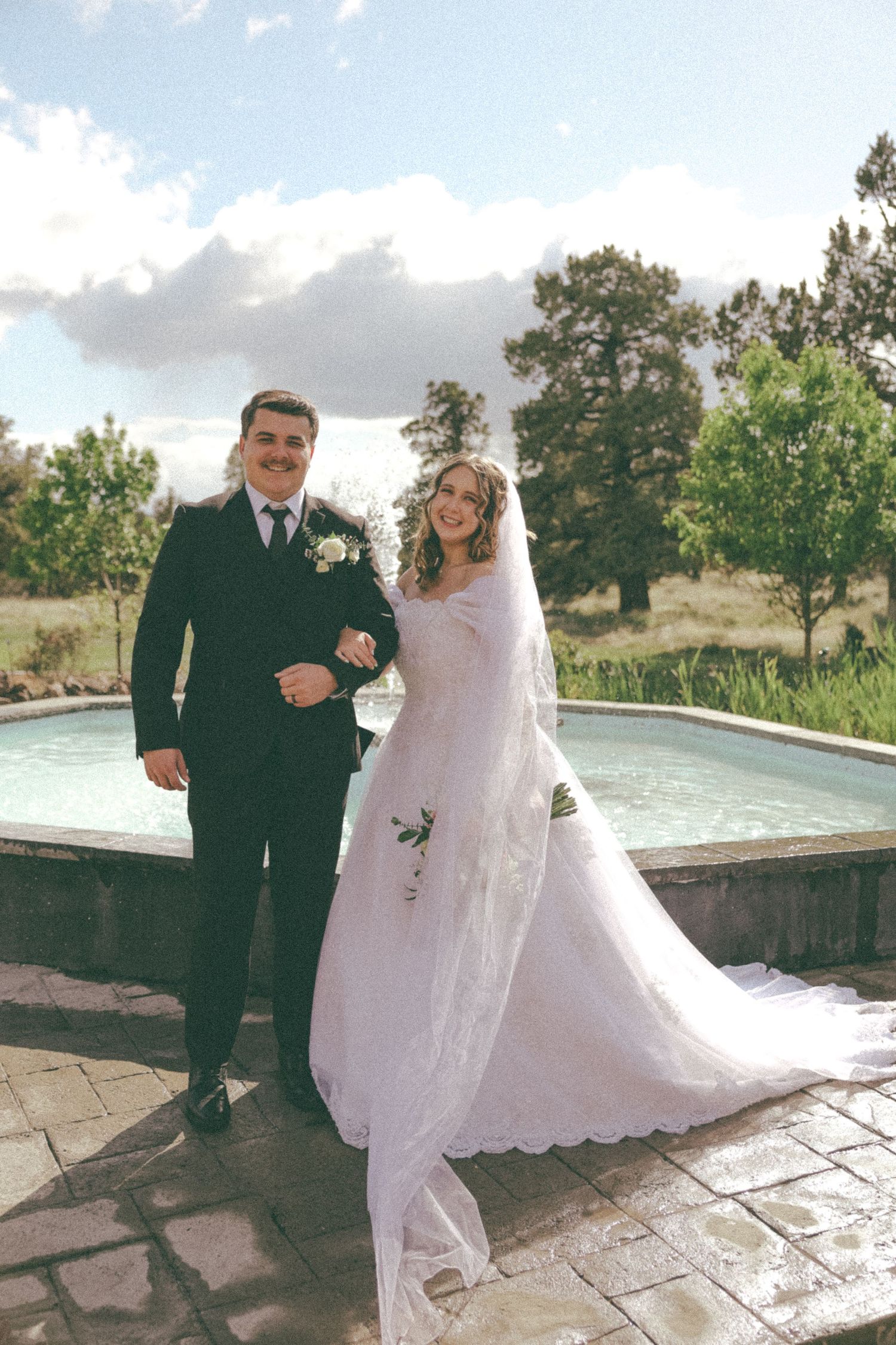 Newlyweds posing by ornamental pool on stone patio during sunset photo session.