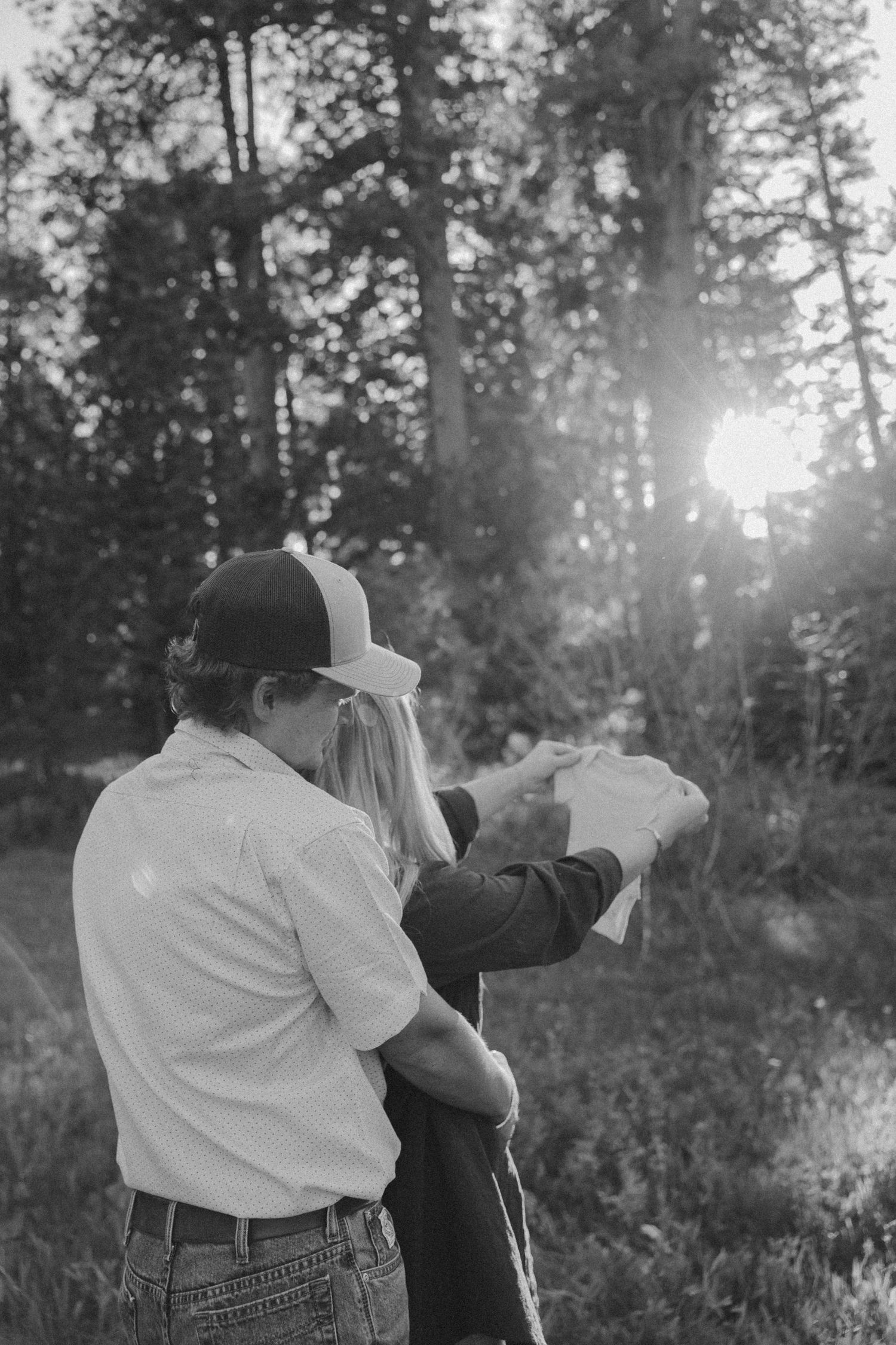 Silhouetted figures embracing at sunset with sunburst through trees.