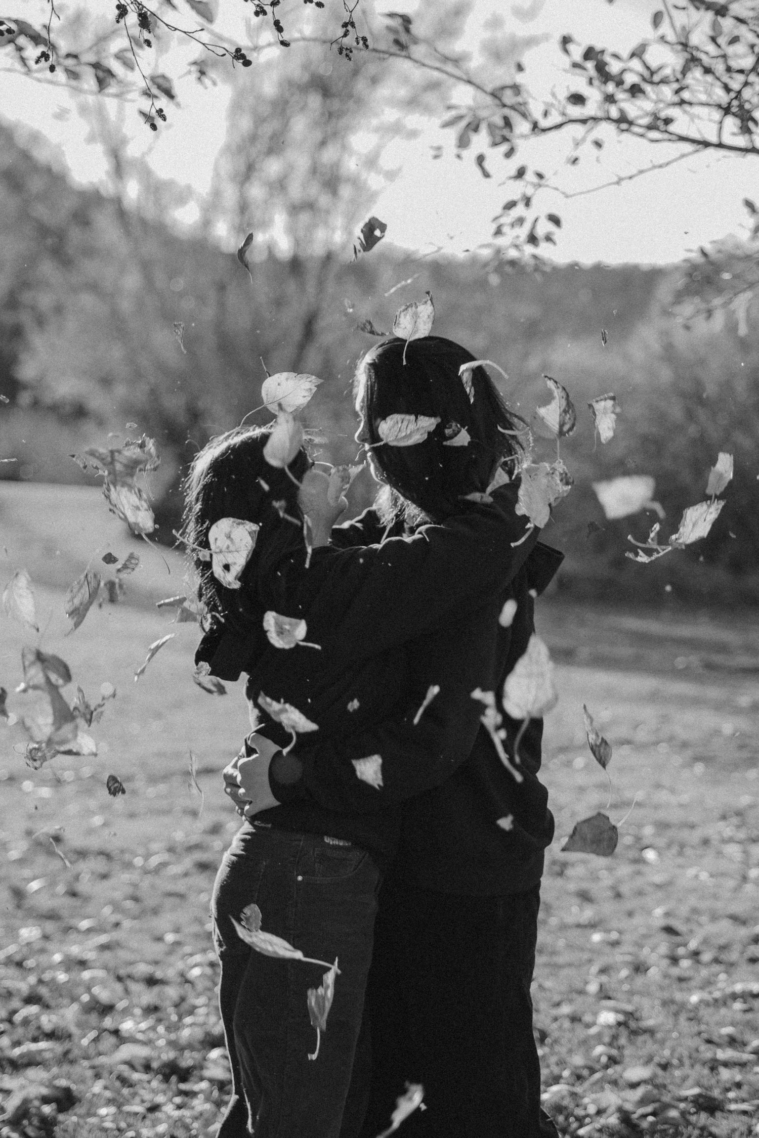 A black and white photograph of autumn leaves falling around a couple embracing in a park setting.