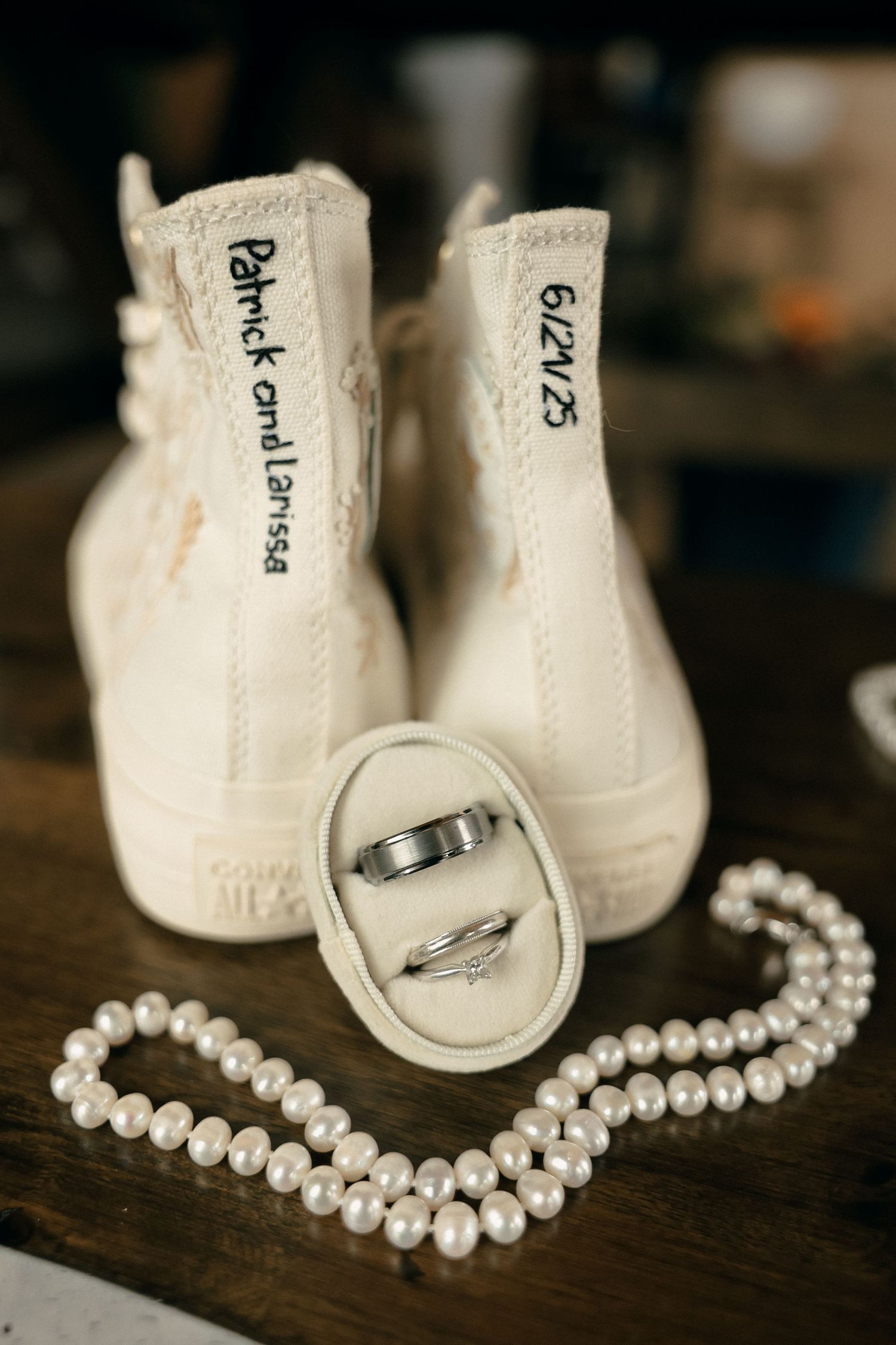 Wedding rings and pearl necklace displayed with white canvas shoes on a wooden surface in a vintage style setup.