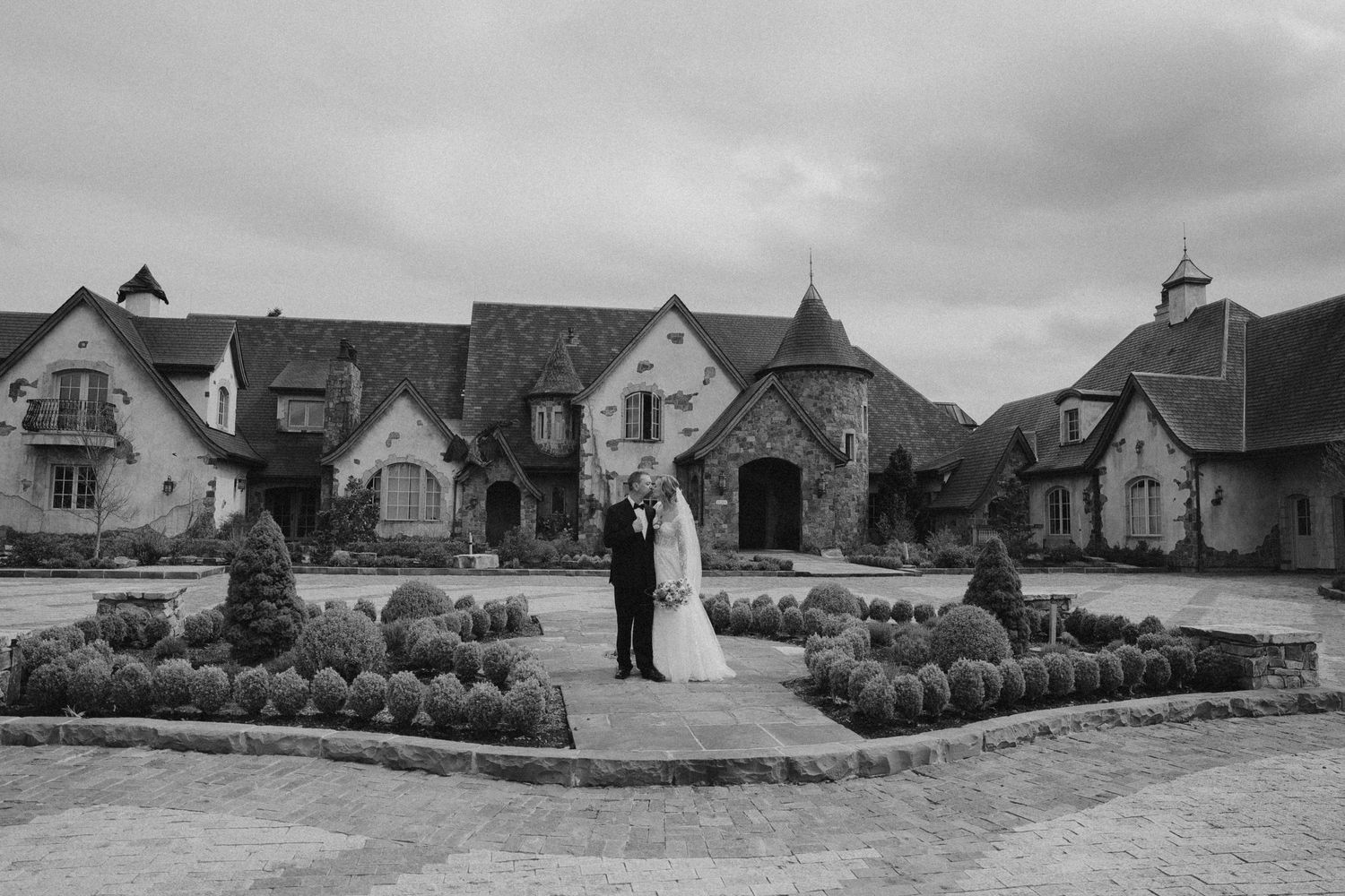 Monochrome wedding portrait of couple standing at center of grand estate entrance.