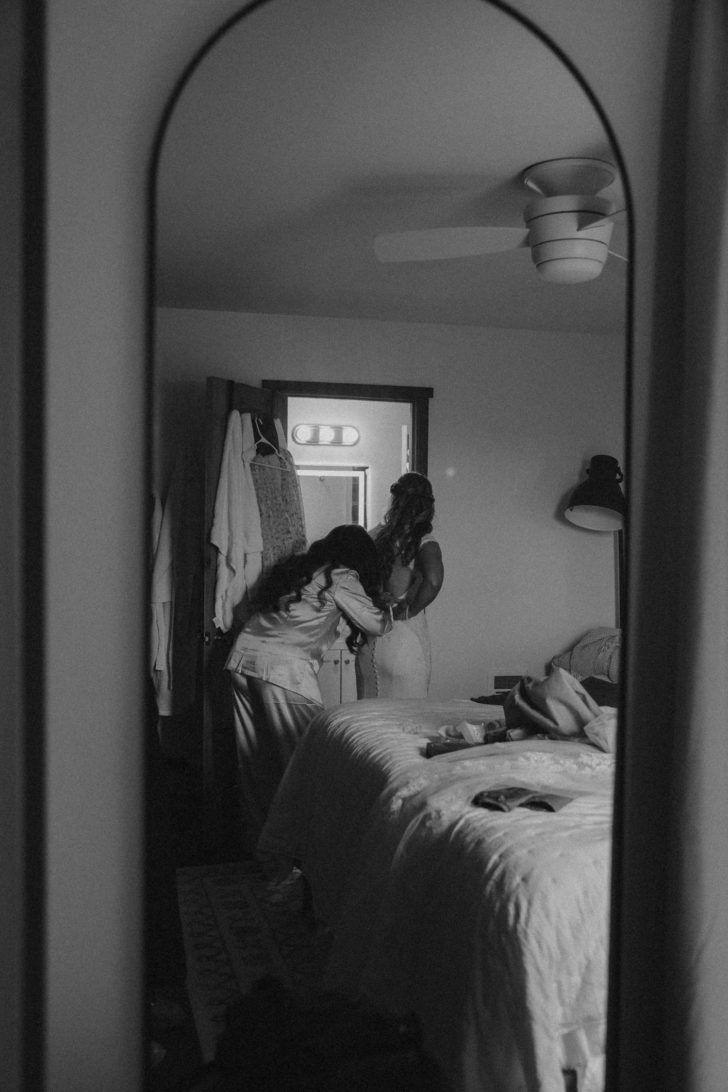 Black and white reflection of morning wedding preparation scene in an arched mirror showing a bedroom interior.