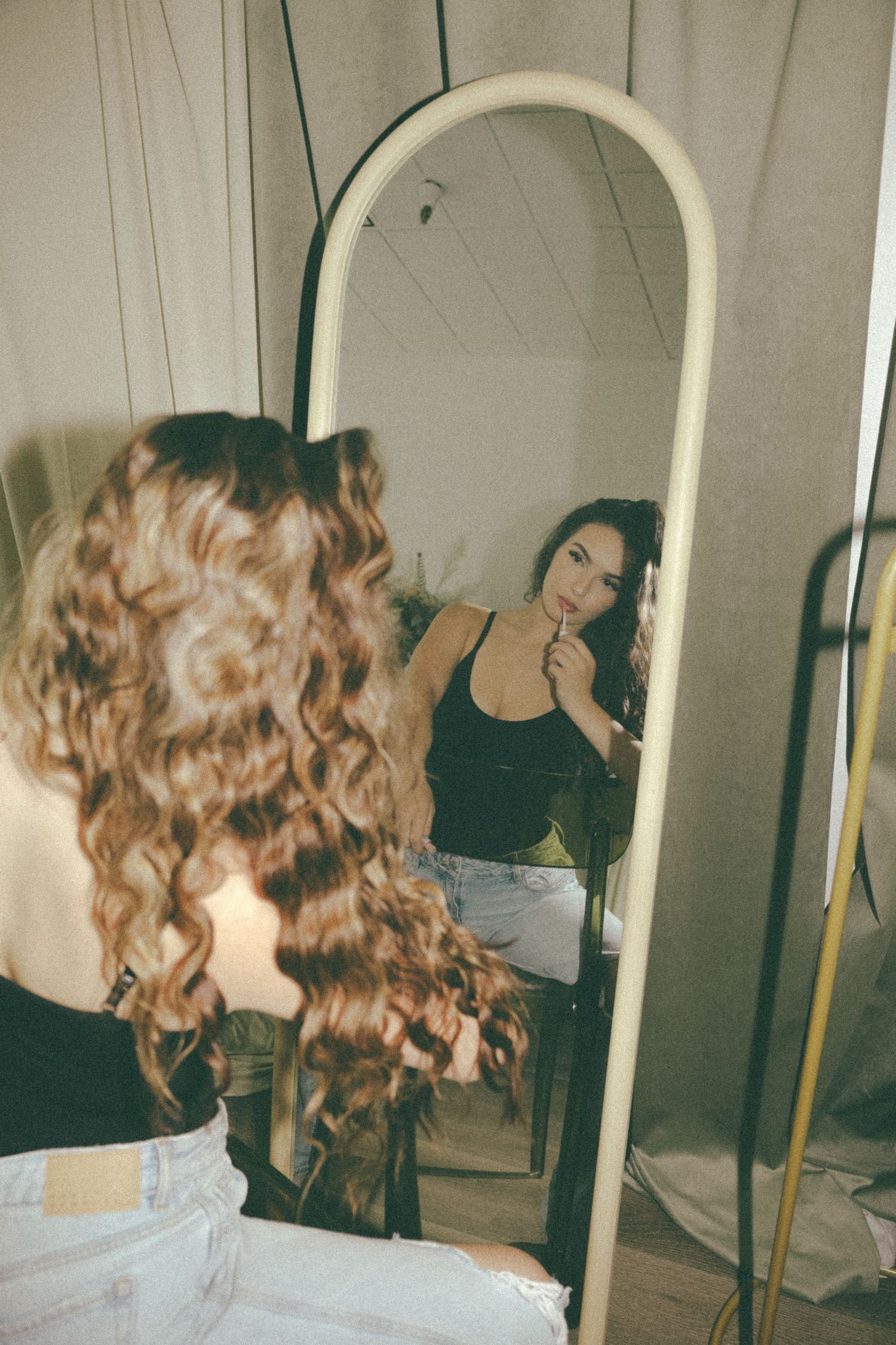 Vintage-style mirror reflection photo showing long curly hair and casual outfit.