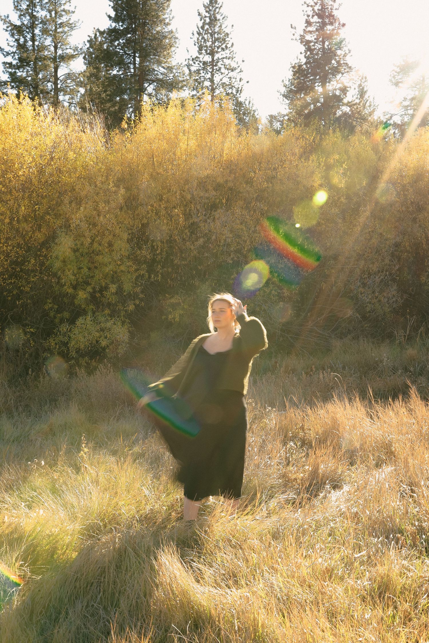 A figure twirls in a black dress amidst sun-drenched autumn grass.