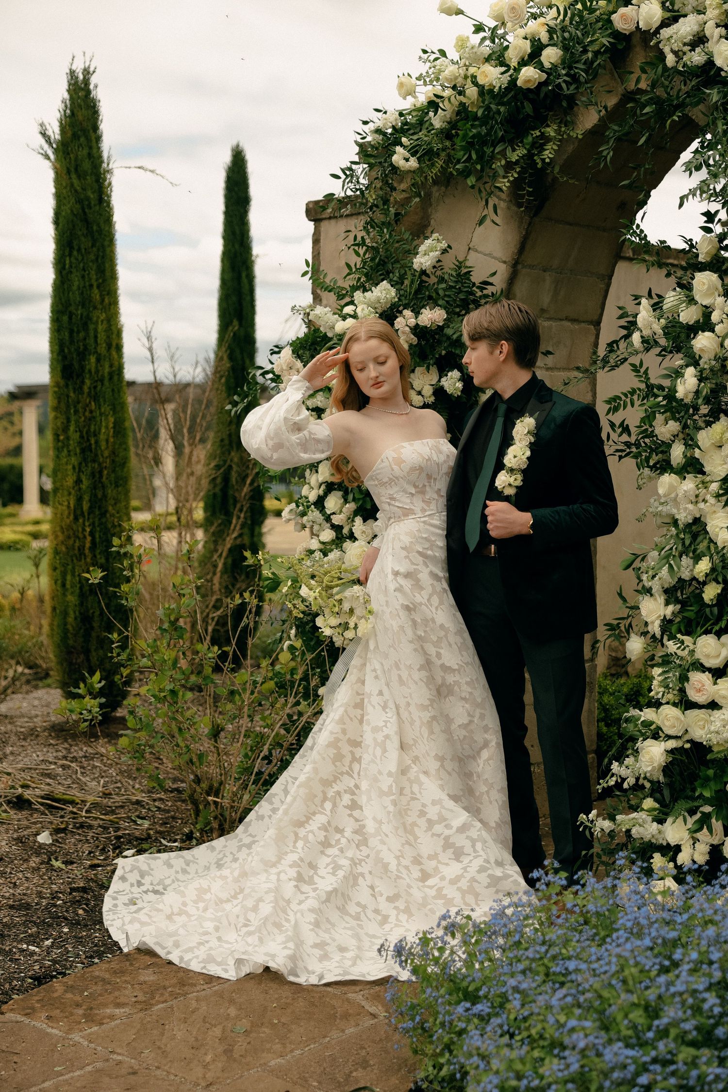 Wedding portraits in a garden setting with floral arch and bluebonnets in bloom.