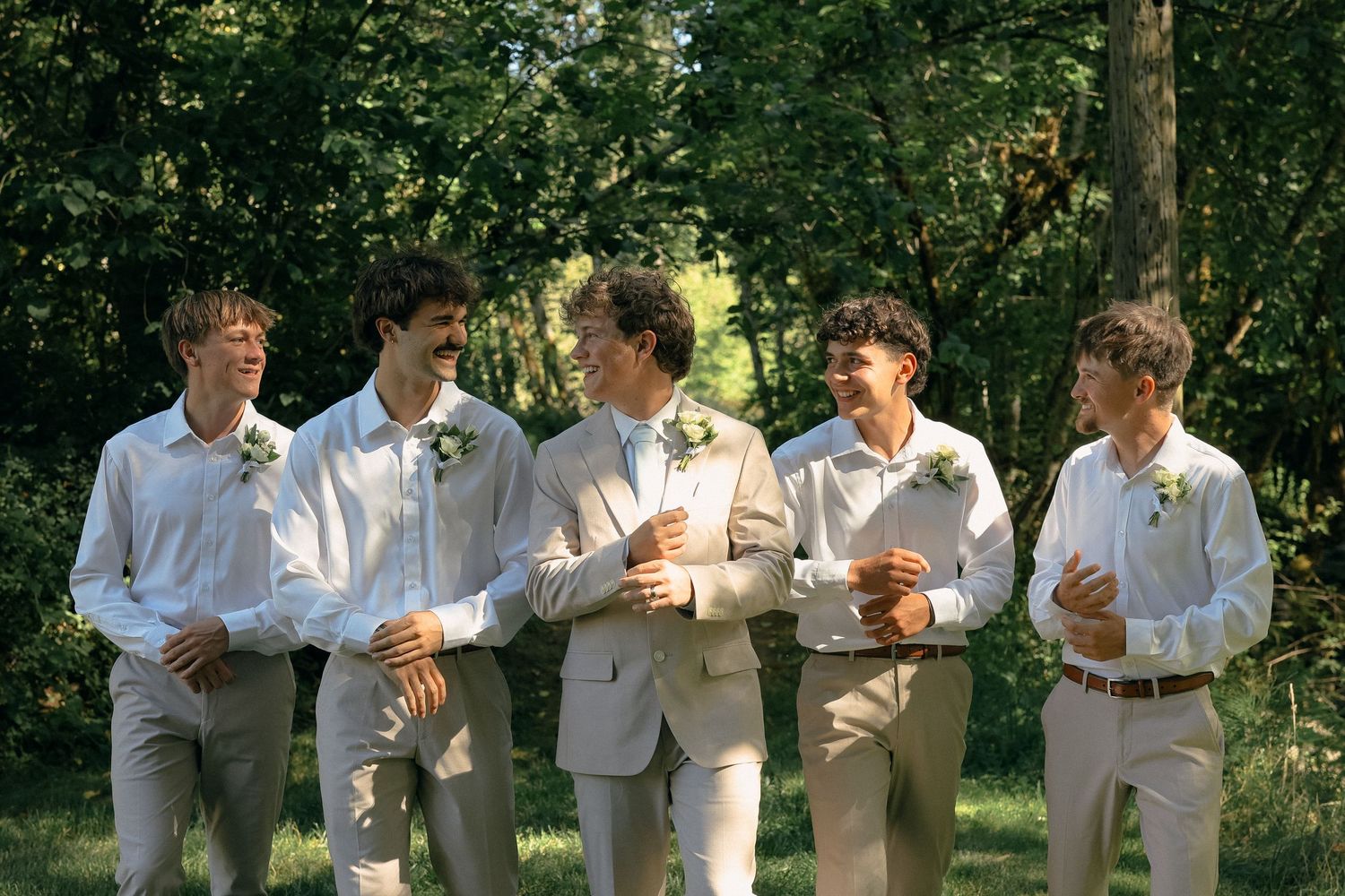 Wedding party members in white and tan attire toast with champagne glasses in an outdoor garden setting.