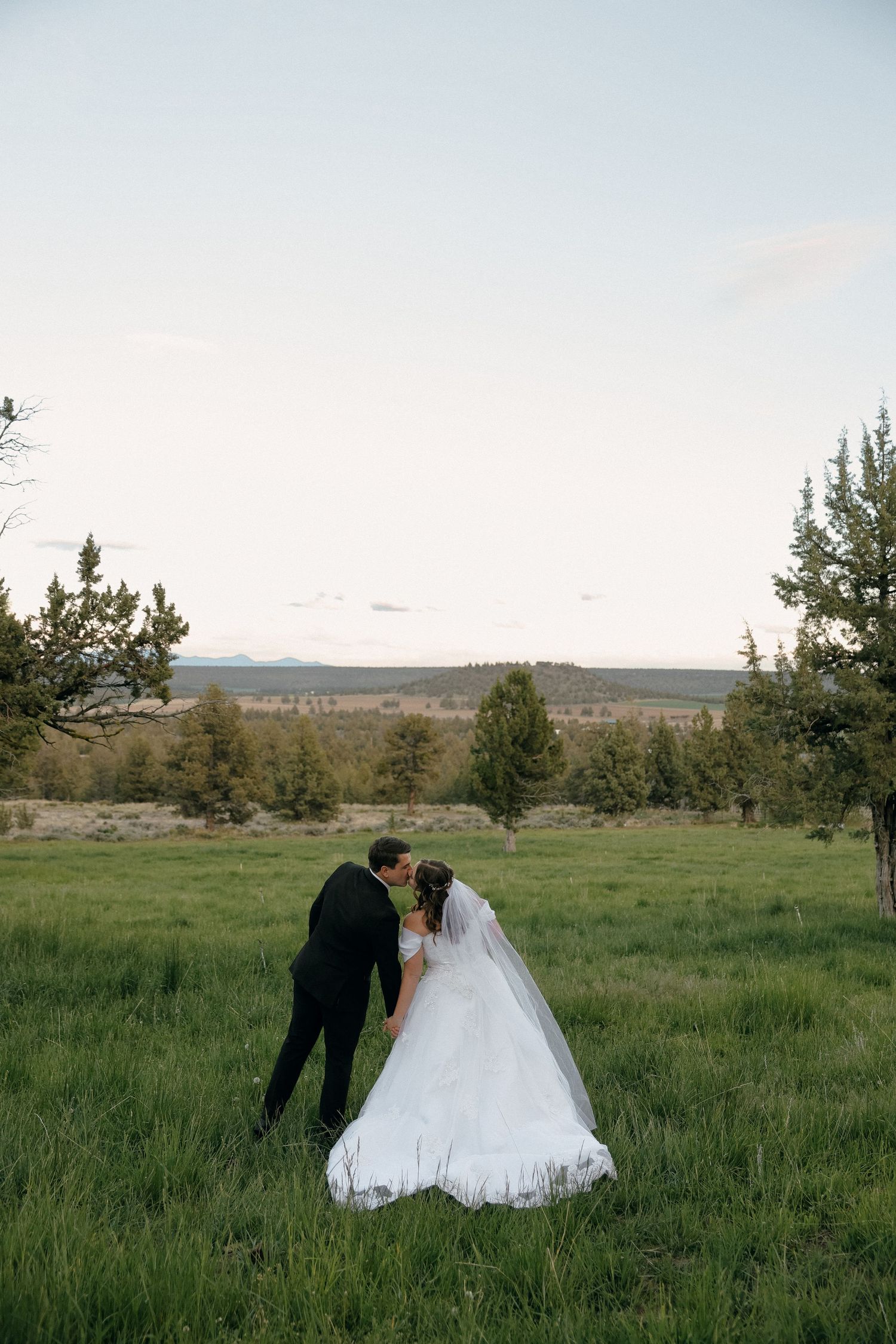 Couple sharing intimate moment in scenic field during sunset wedding photoshoot.