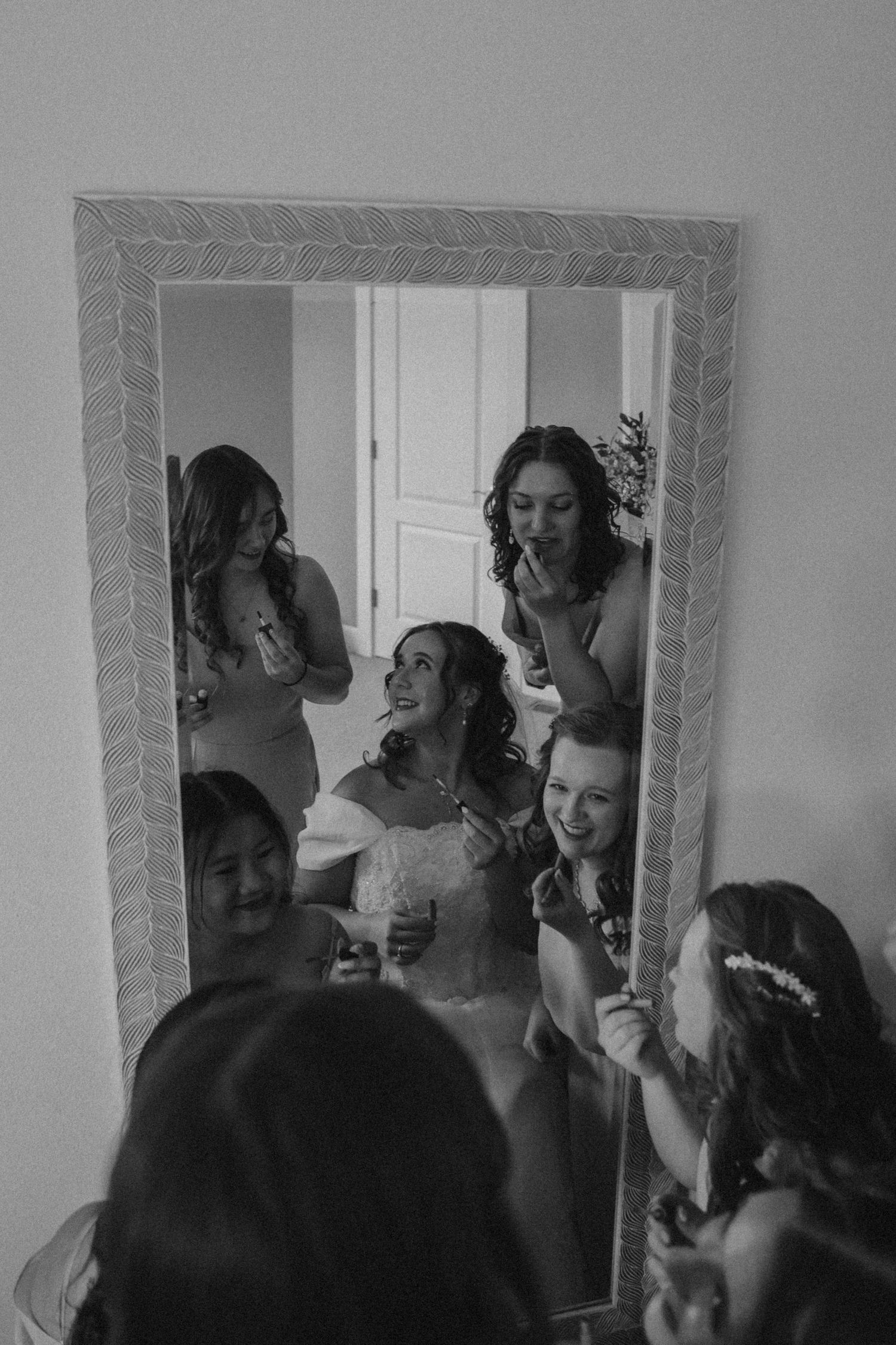Wedding party members preparing and laughing together in front of mirror.