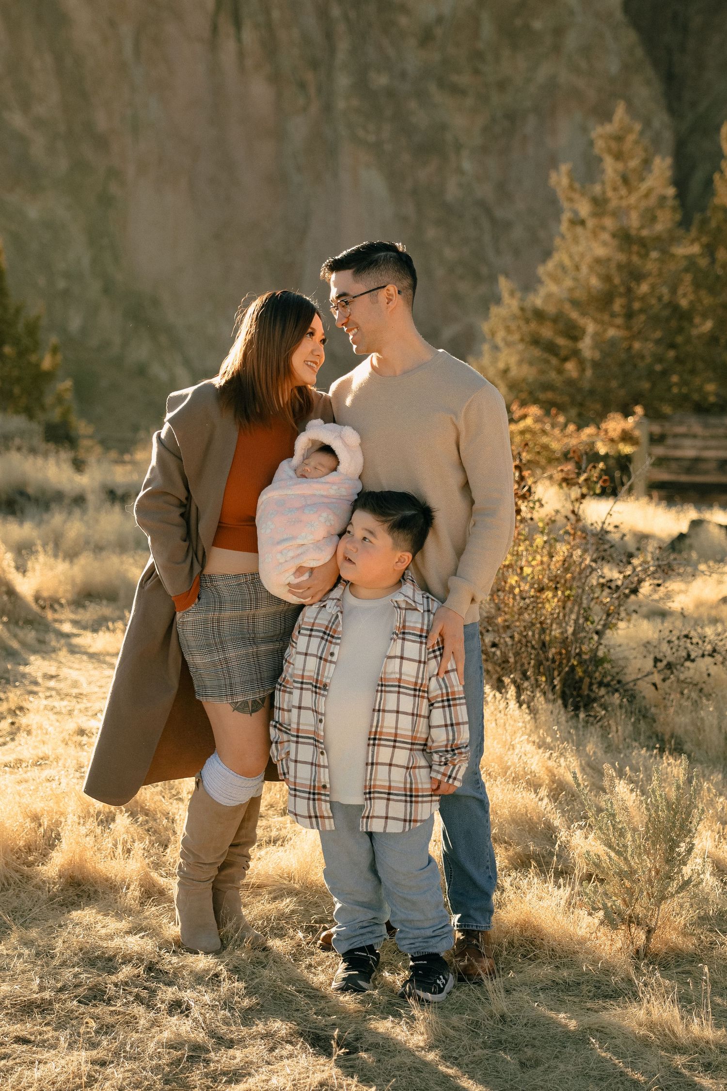Young family poses together against rocky mountain backdrop in warm sunlight.