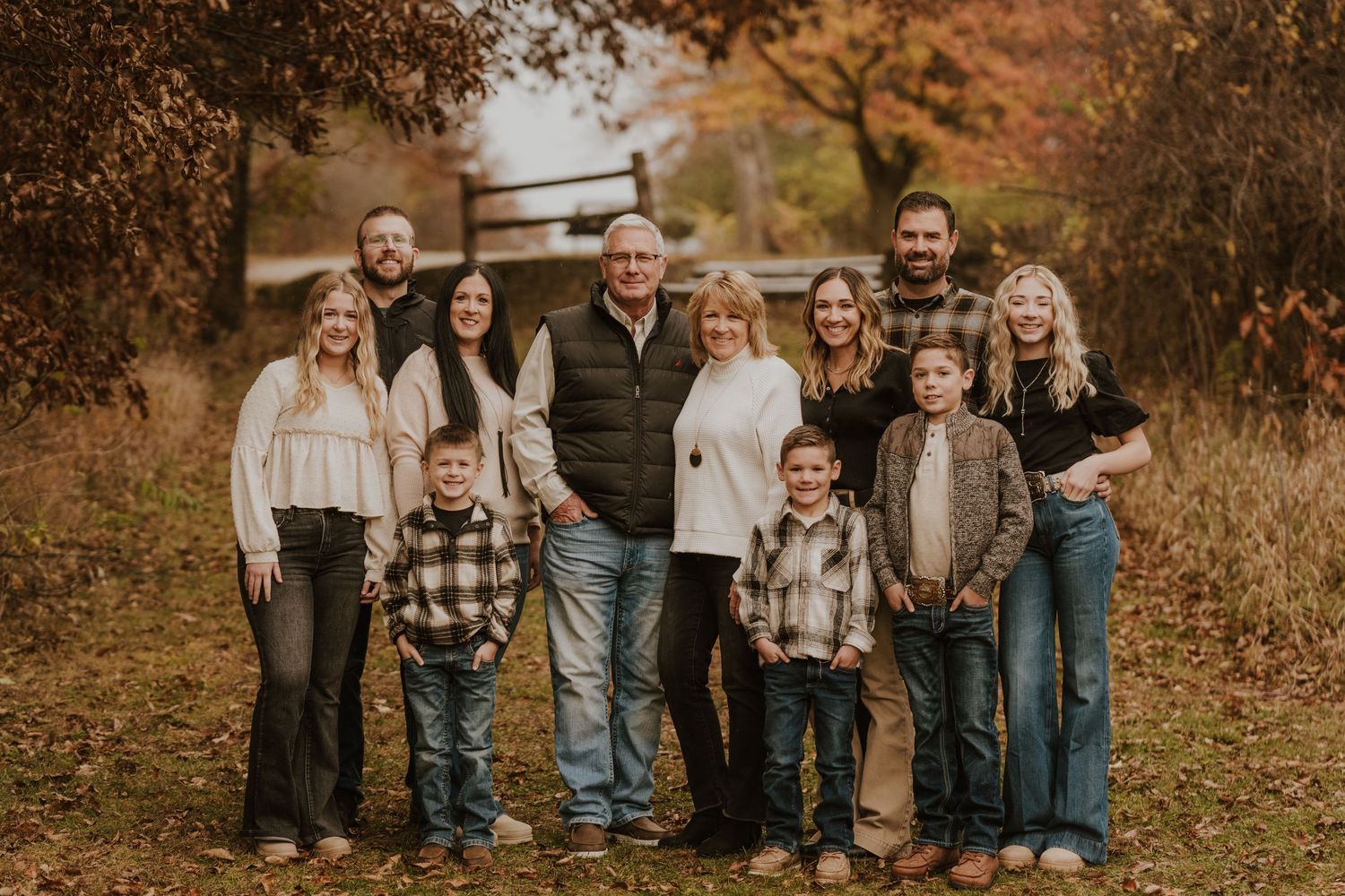 Multi-generational family poses outdoors together on an autumn day with fall foliage in background.