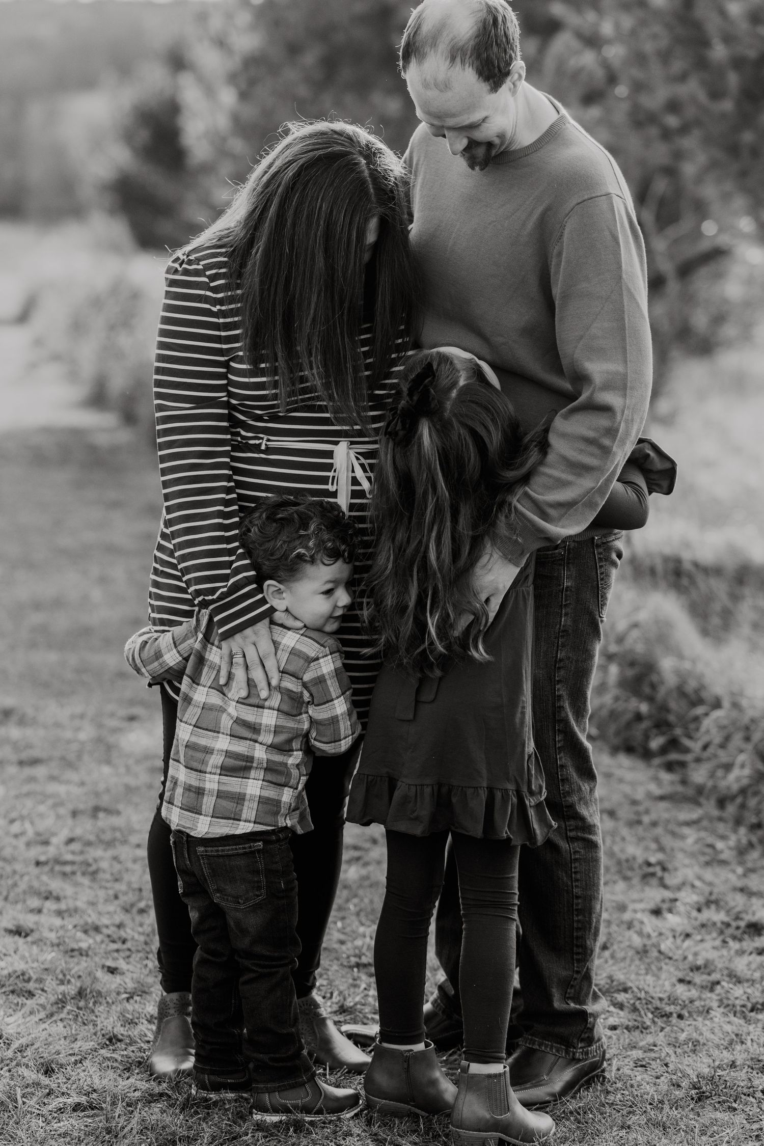 Black and white portrait of a family embracing outdoors in a heartwarming candid moment.