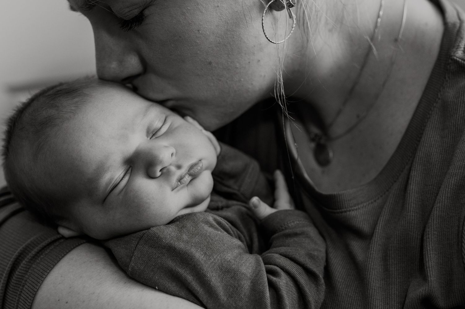 A tender black and white portrait captures an intimate moment as a baby naps peacefully on mom's shoulder.