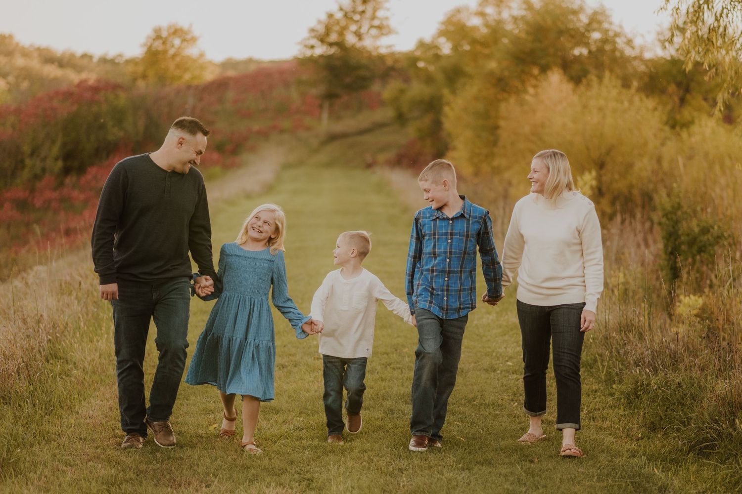 A family walking together at sunset through a grassy meadow with autumn colors in the background.
