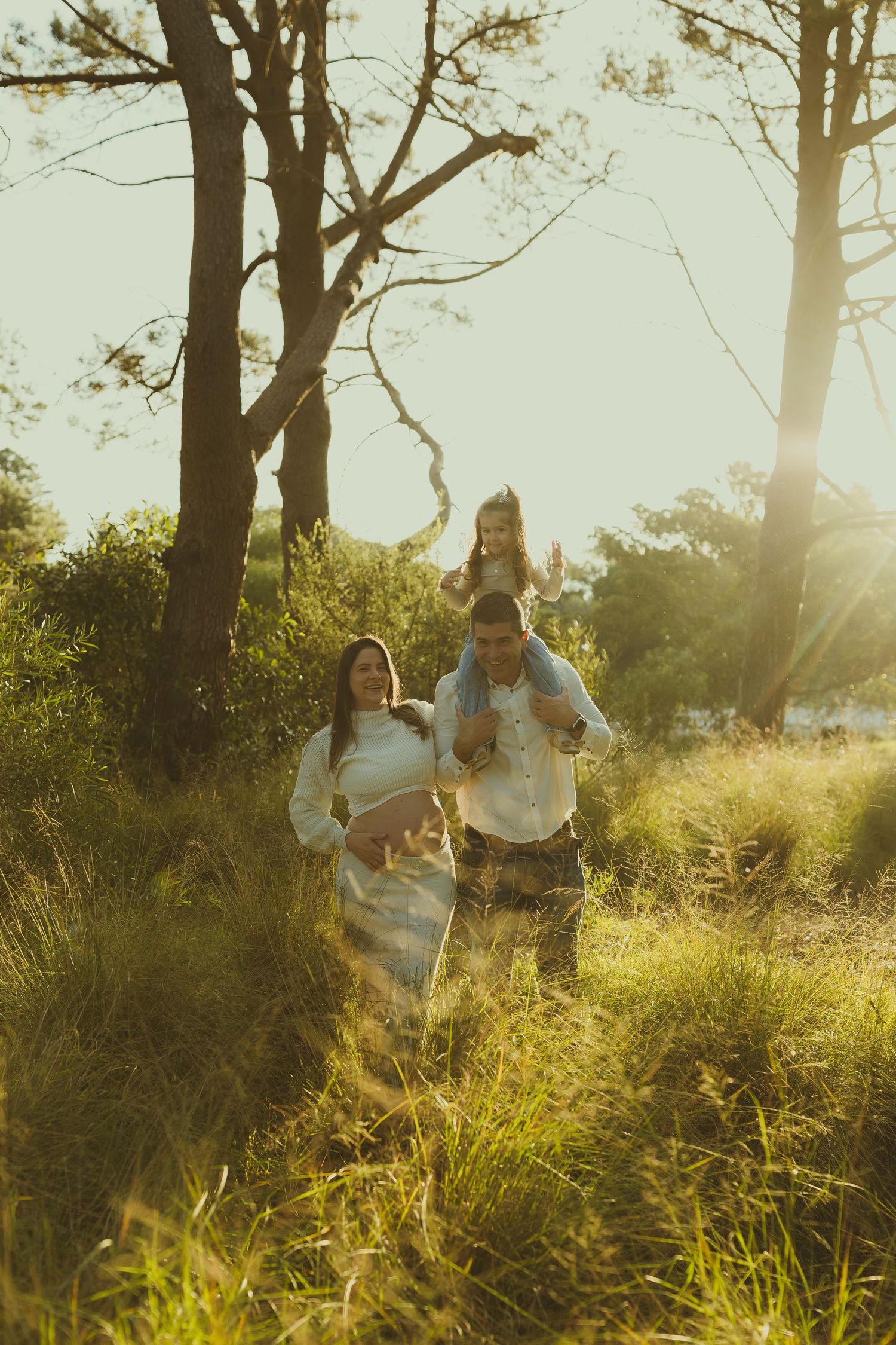 Family enjoying a golden sunset moment in tall grass with soft backlighting creating a warm ethereal atmosphere.