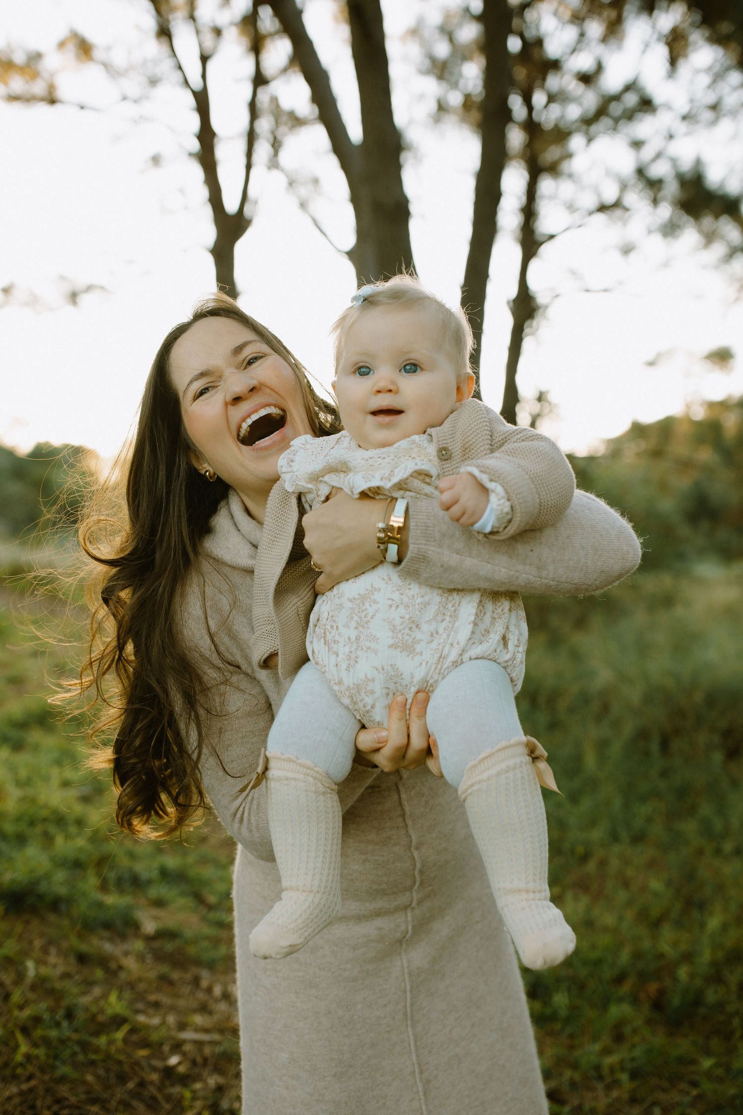 Joyful parent and baby sharing playful moments together outdoors in matching beige outfits.