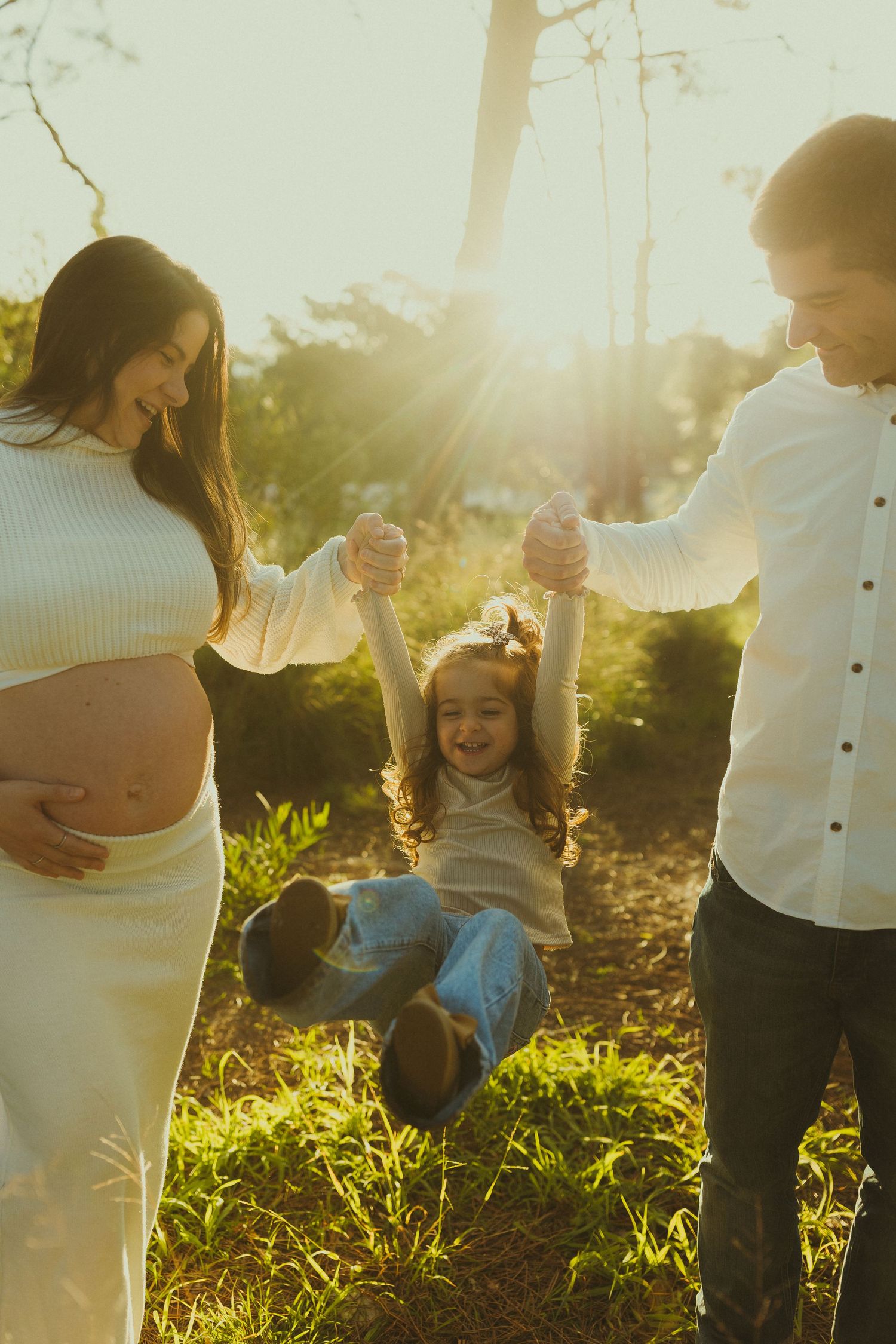 Parents playing with child in sunlit meadow during golden hour photoshoot.