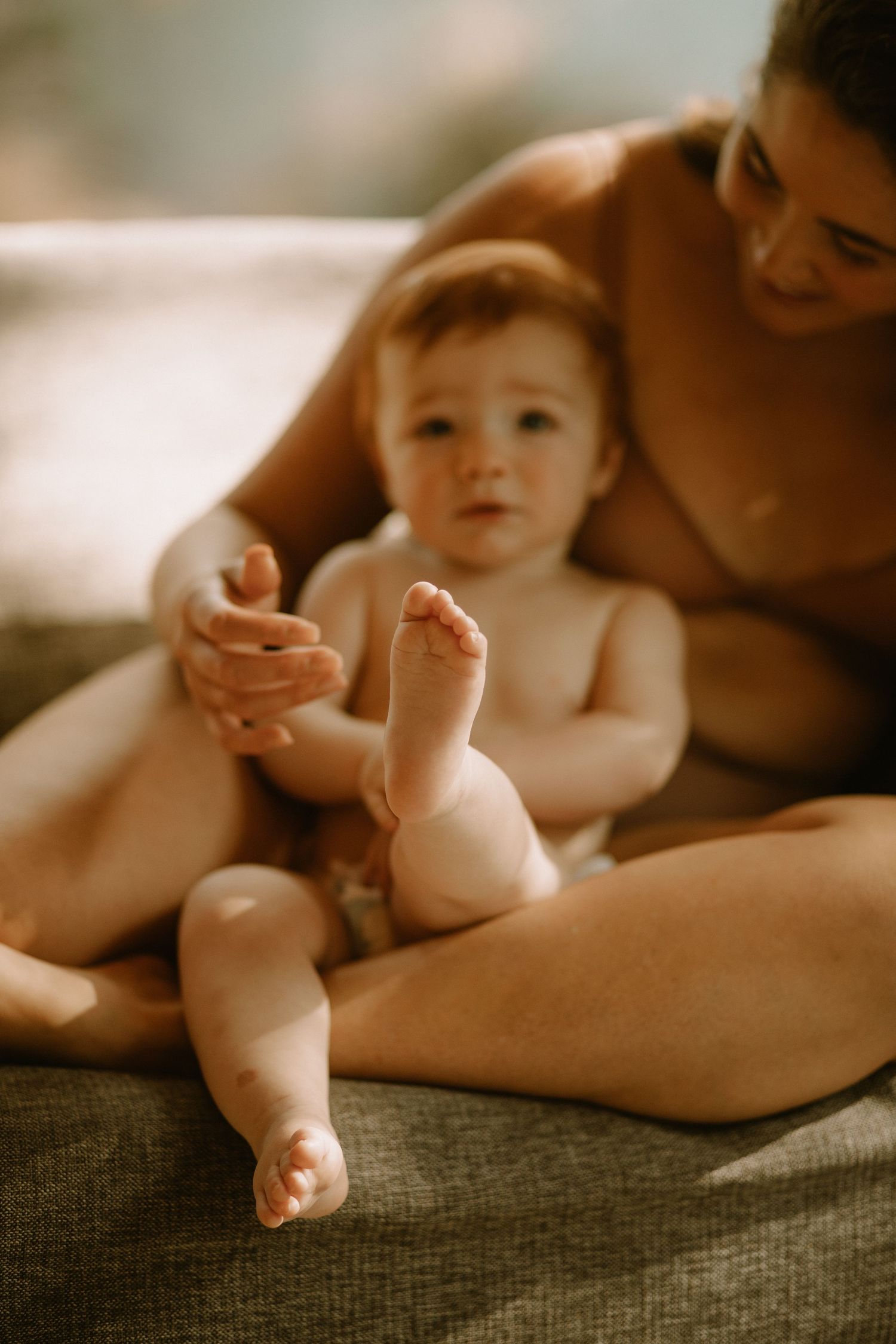Baby with tiny toes and feet resting on a gray couch while being held in a warm, intimate setting.