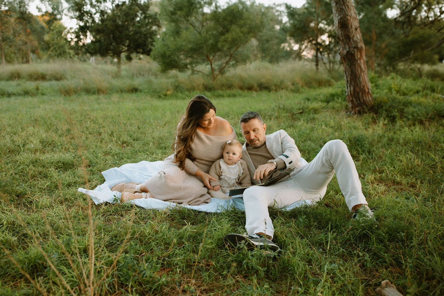 Couple relaxing together on white blanket in grassy meadow during golden hour sunset.