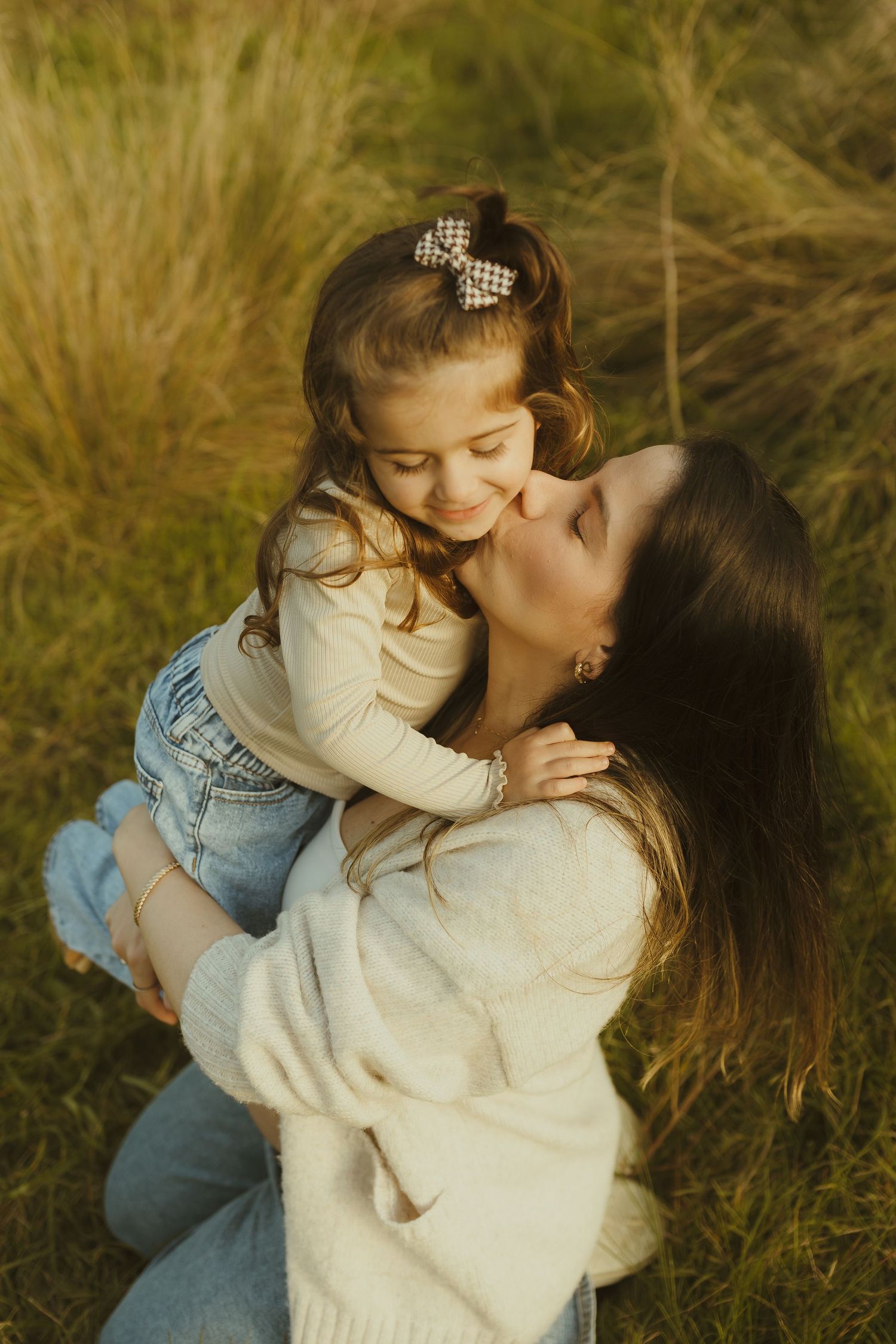 Sweet candid moment between parent and child embracing in golden sunlit field.