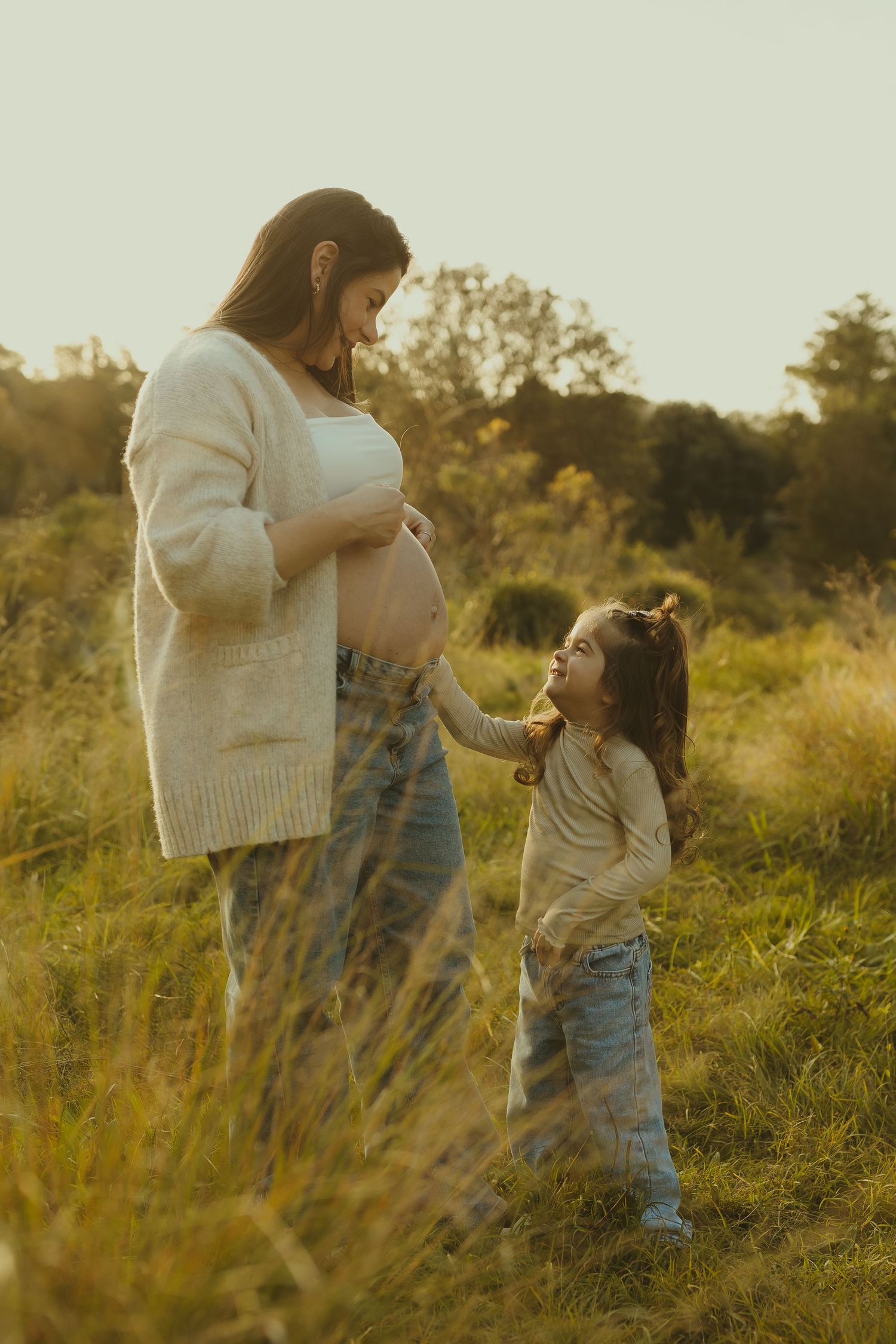 Heartwarming moment between expectant mother and young child in golden field at sunset.