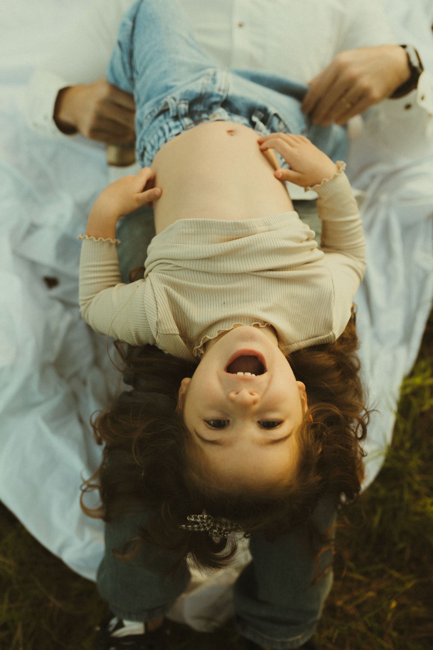 Joyful child lying on blanket outdoors with playful upside-down pose during family photoshoot.