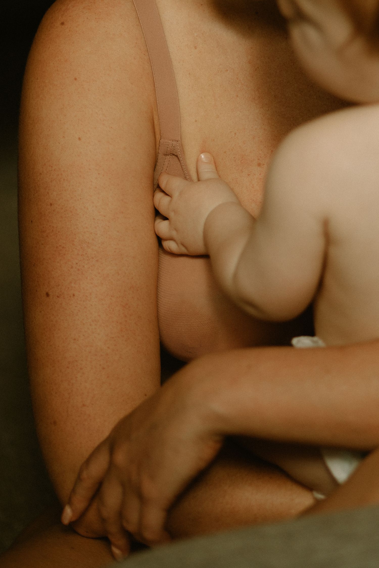 Close-up shot of tiny baby hand grasping adult arm in warm lighting showing tender moment of connection.