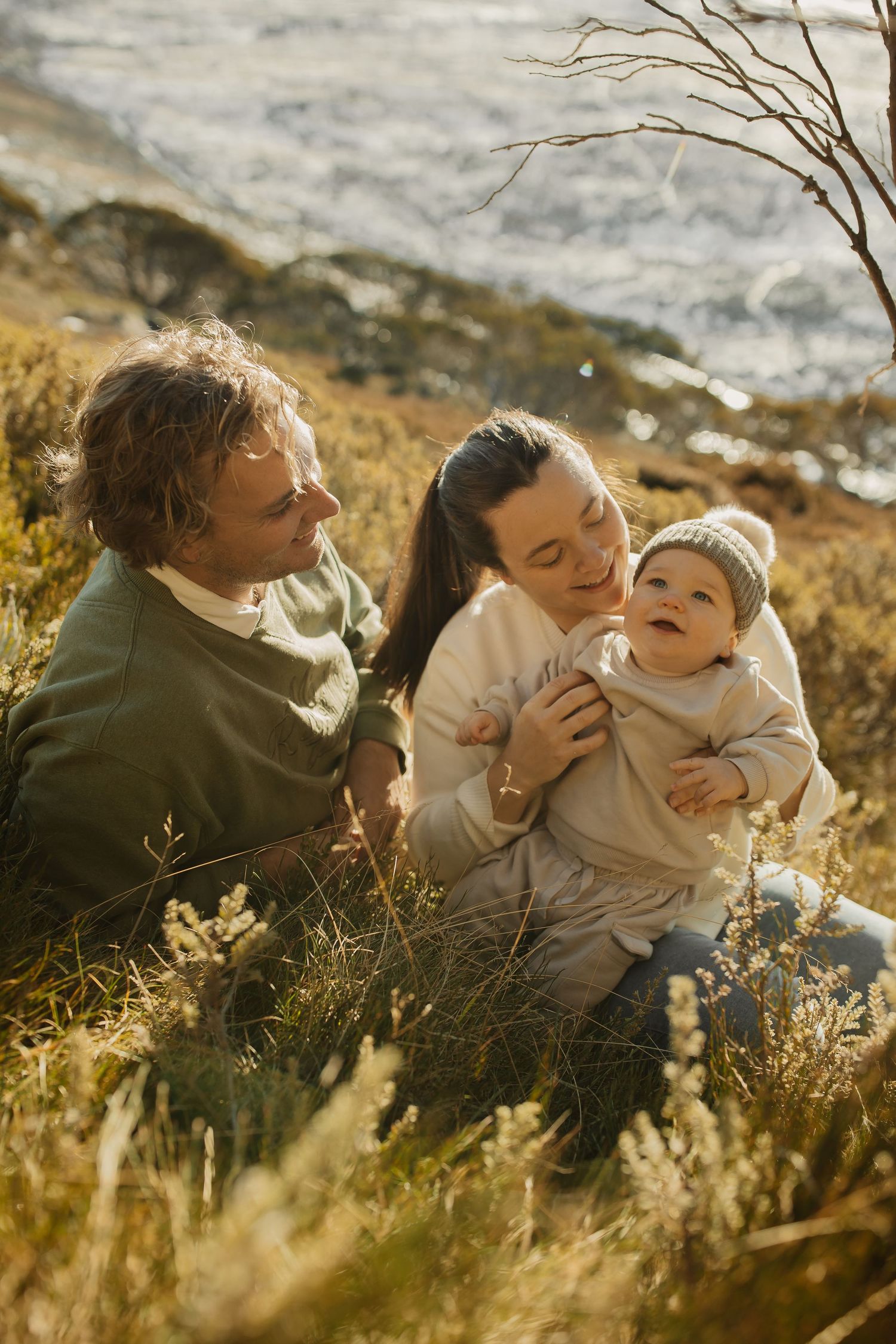 A family sits together in golden sunlit grass near the coast during a warm afternoon.