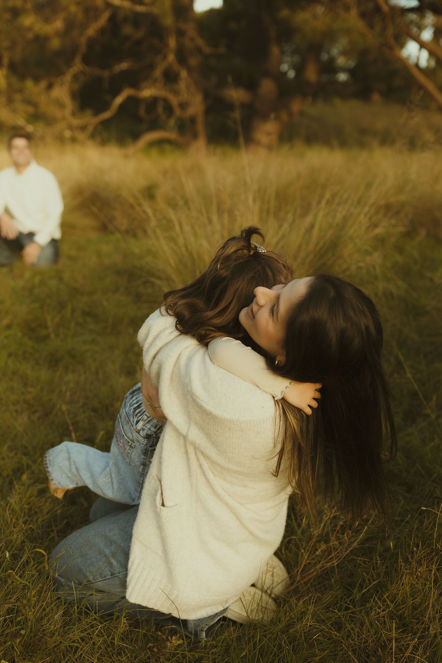 Candid embrace between two people sitting in golden grass during sunset photoshoot.