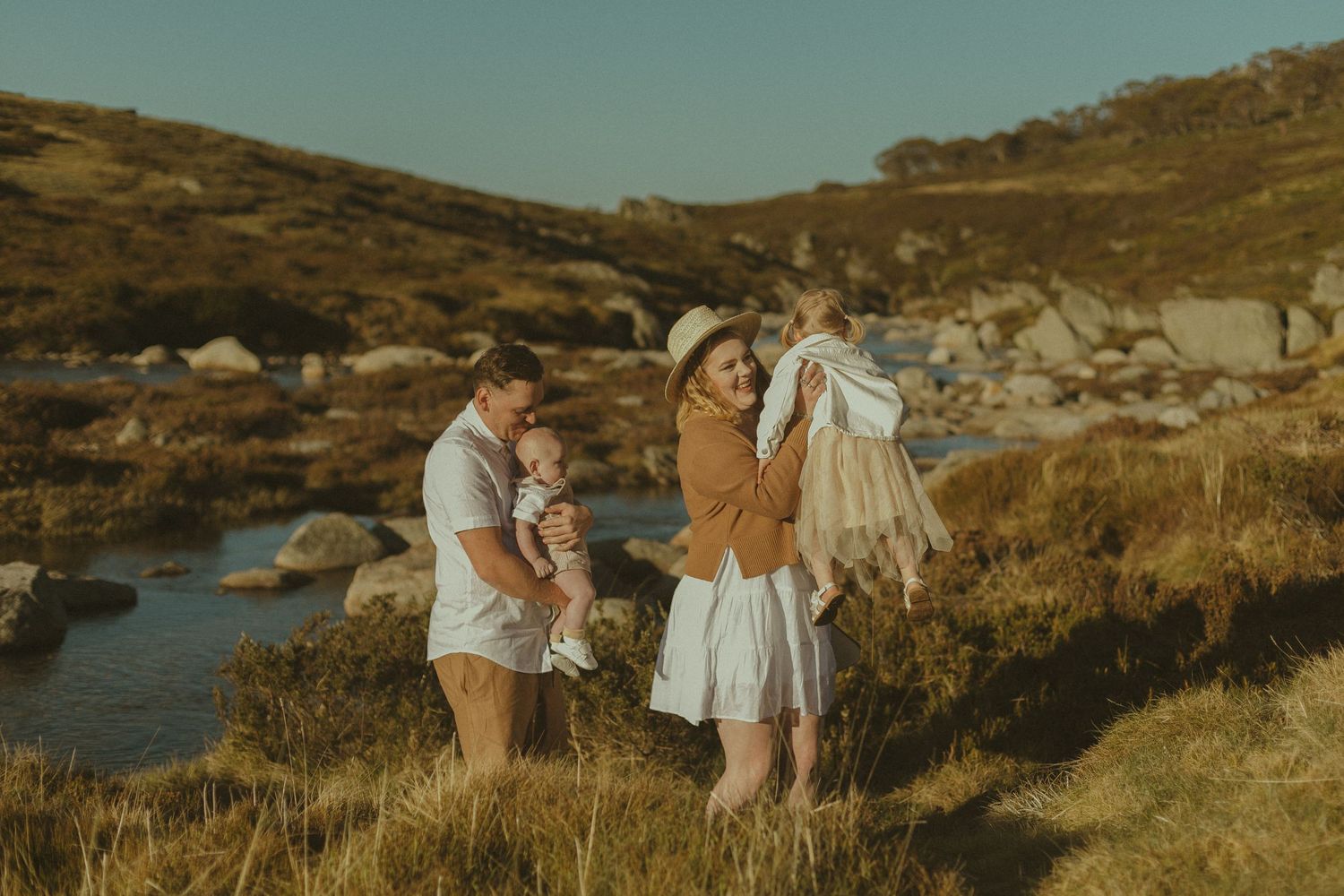 Group enjoying an outdoor adventure in a scenic mountain landscape with a stream at golden hour.