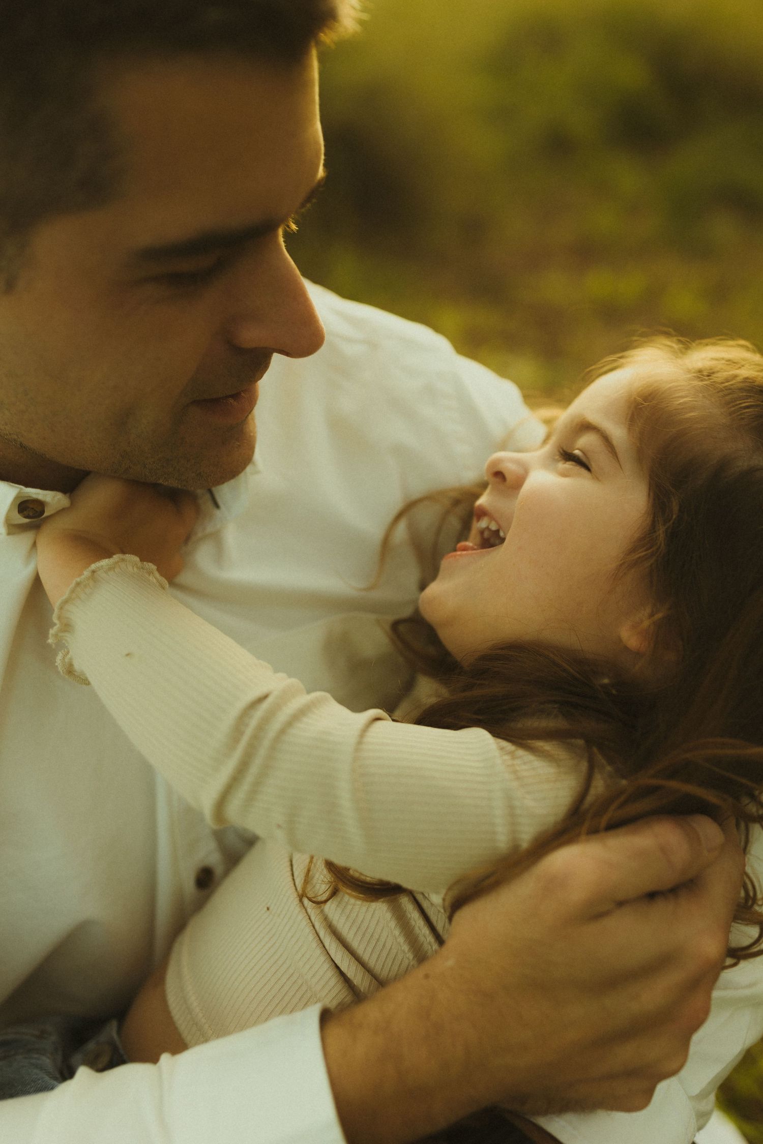Intimate moment between parent and child sharing laughter in warm sunlit setting.