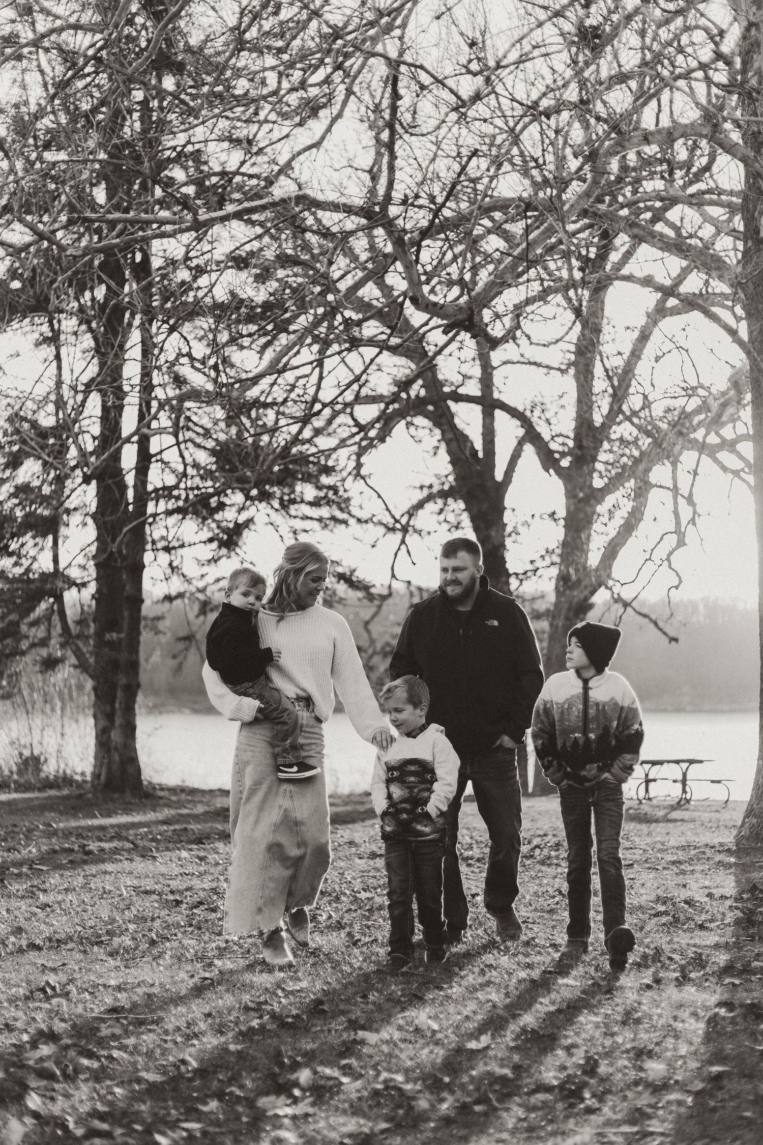Family silhouettes gather under bare winter trees on misty afternoon.