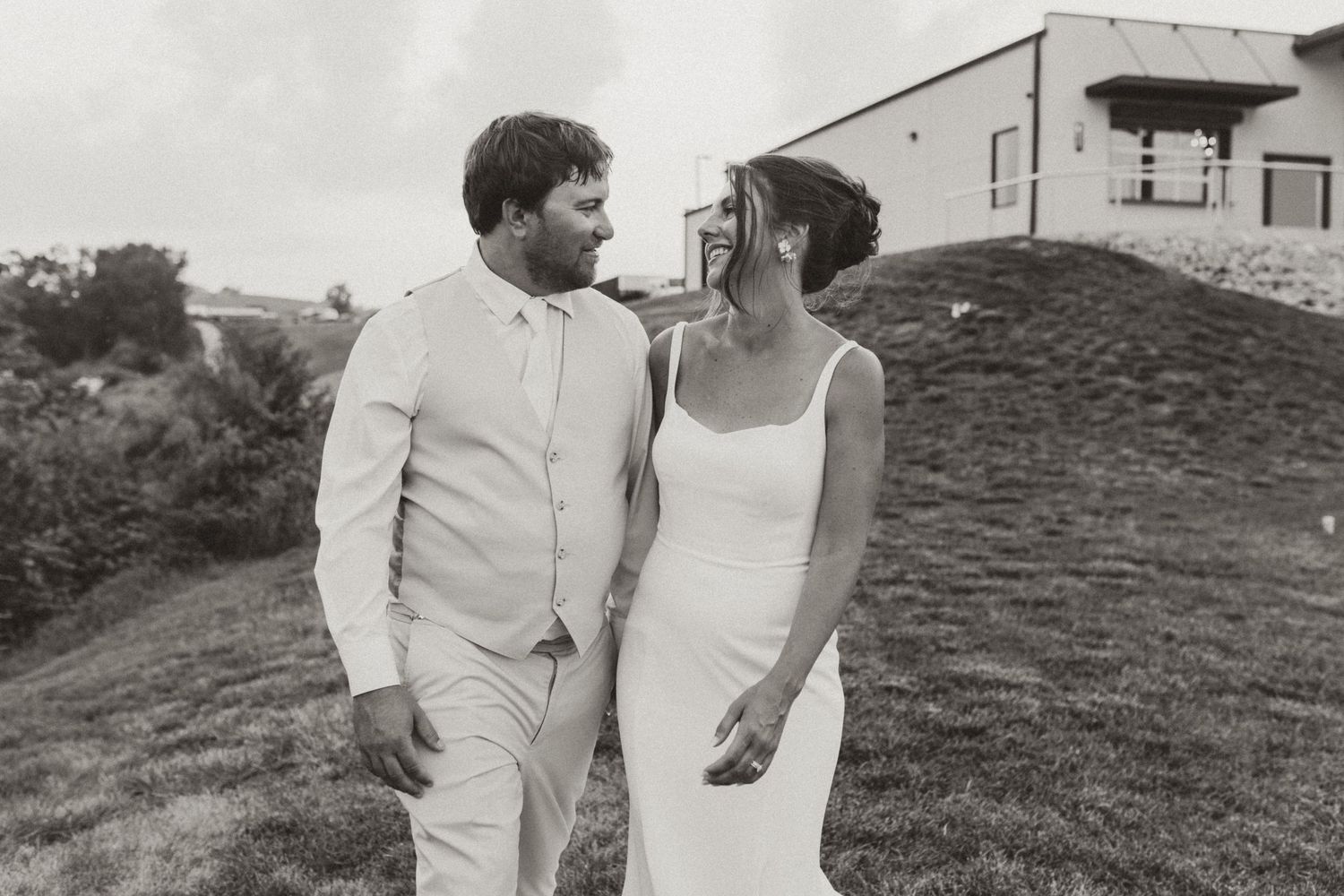 Black and white portrait of couple in light colored attire sharing intimate moment on hillside.