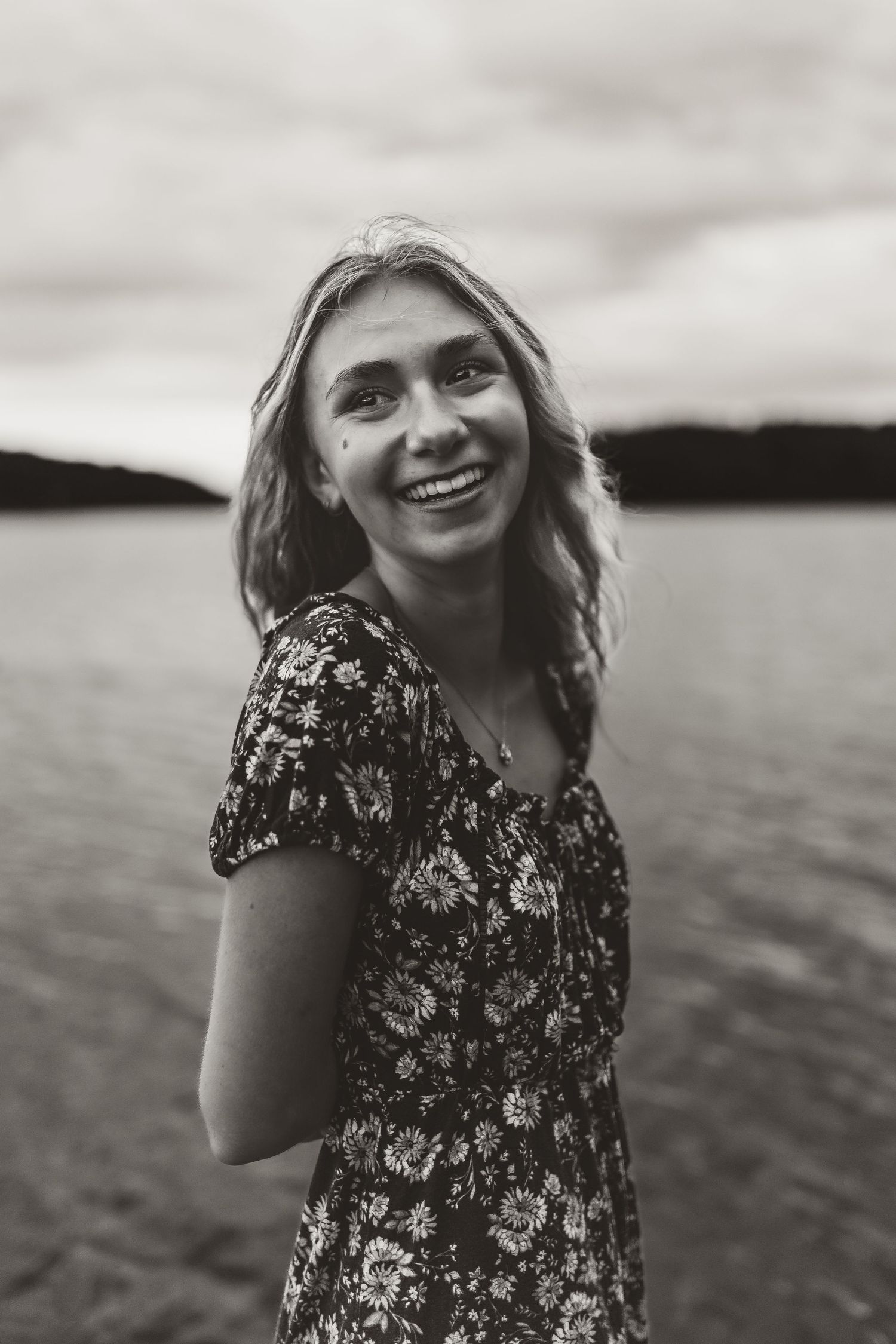 A portrait of someone wearing a floral dress by a lake at dusk.